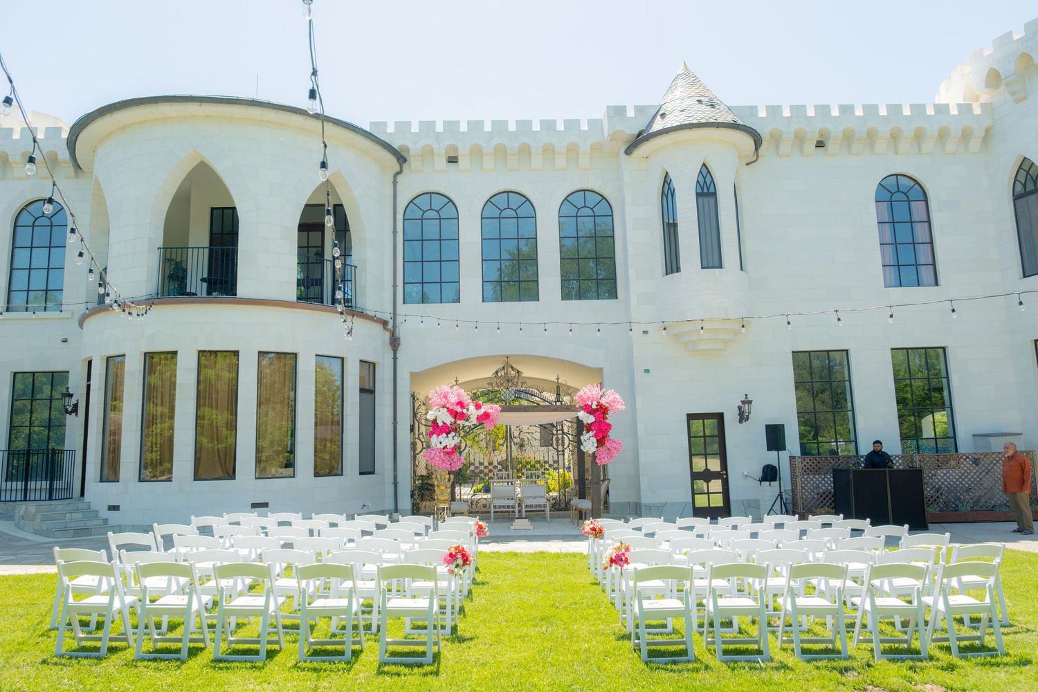 Elegant white castle venue with outdoor wedding ceremony setup featuring white chairs and pink floral decor.