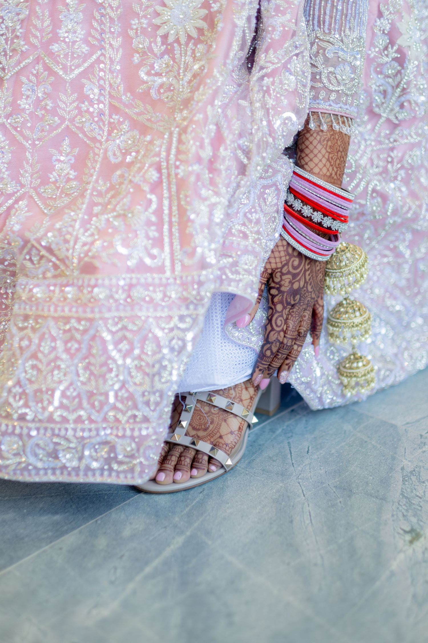 Close-up of Indian bride's henna hands with bangles and embroidered pink lehenga.