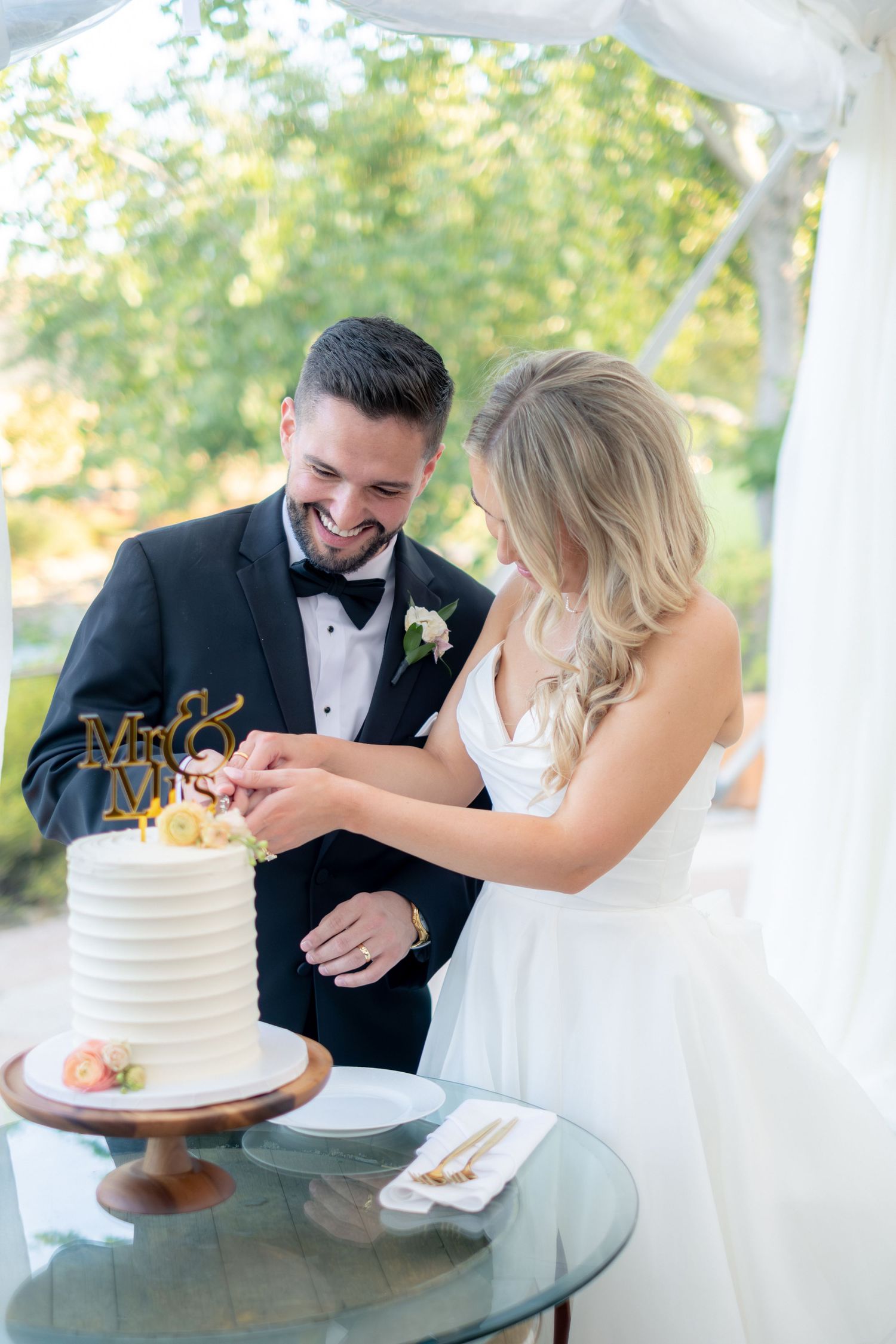Happy bride and groom cut their white single-tier wedding cake with Mr and Mrs gold topper.