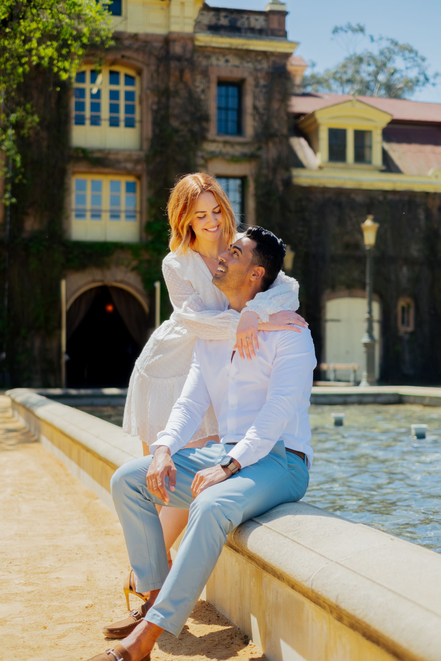 Happy couple embracing by a fountain in front of a charming ivy-covered historic building.