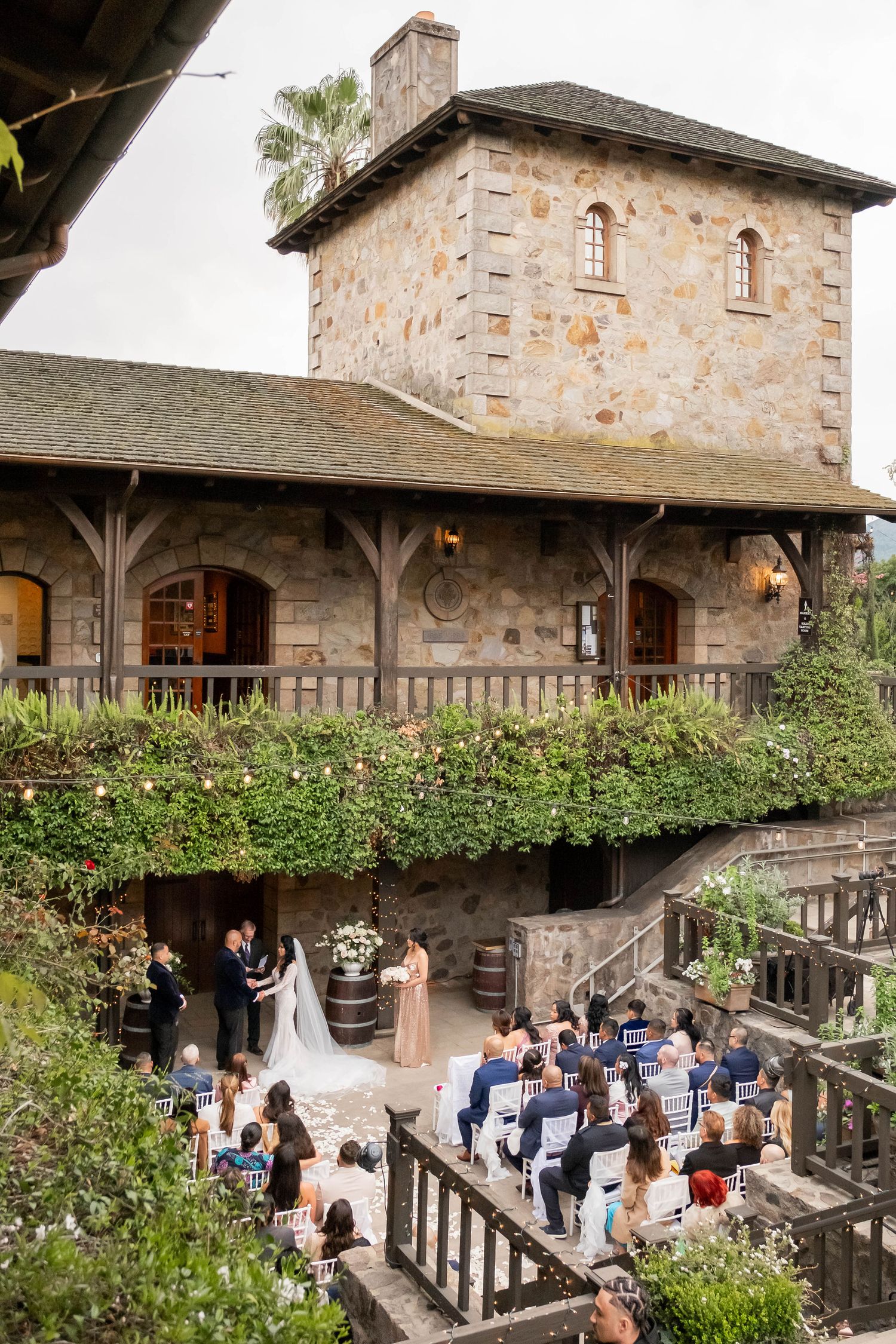 Aerial view of a wedding ceremony at a stone castle winery with seated guests.