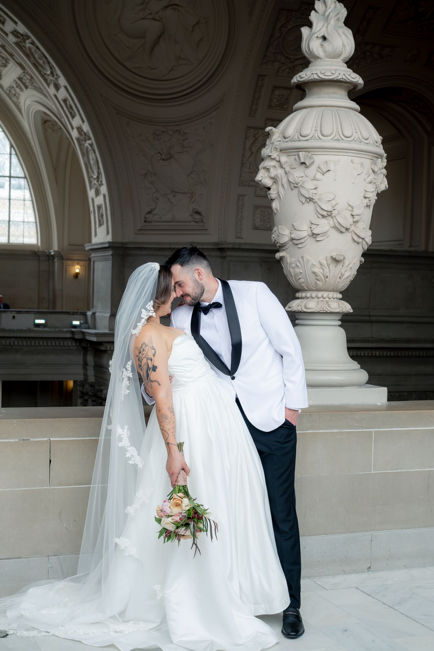 Bride and groom share a romantic moment in San Francisco City Hall, bride in white gown with veil holding bouquet.