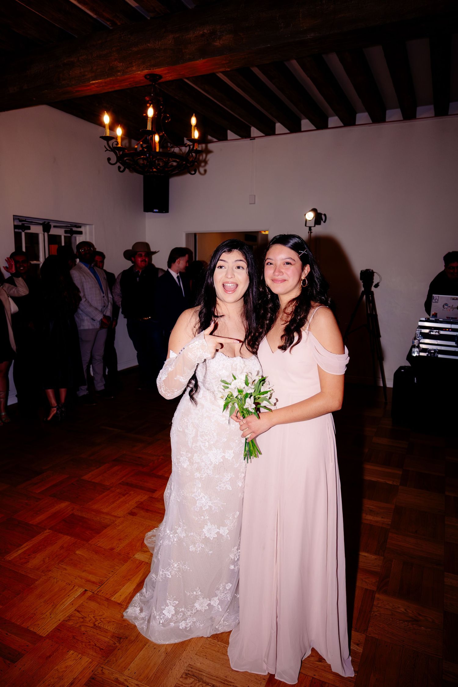 Two bridesmaids in lace and blush gowns pose together on dance floor at wedding reception.