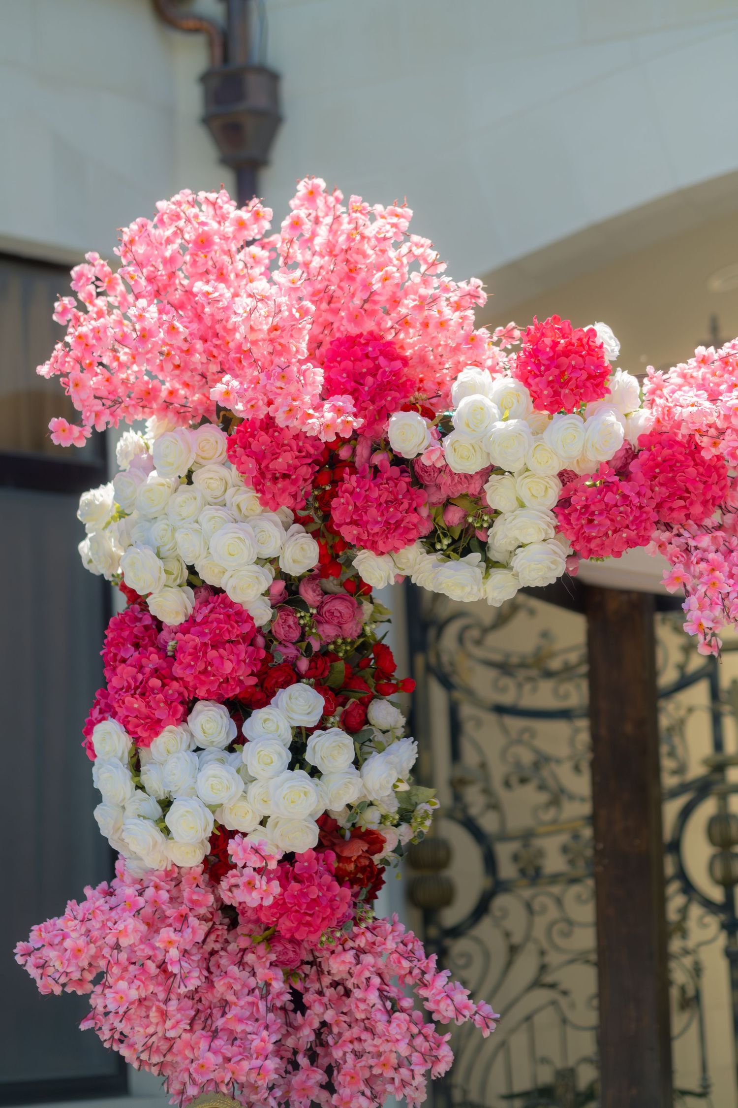 Lush floral wedding arch decorated with pink, red, and white roses and hydrangeas.