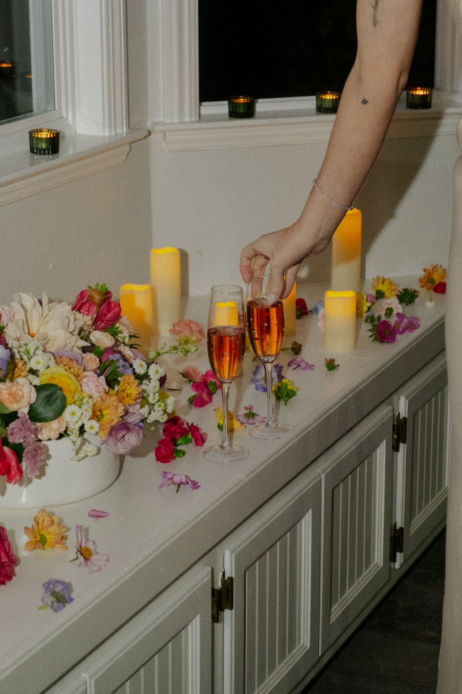 Champagne flutes and candles on white cabinet with colorful floral arrangements at an elegant wedding reception.