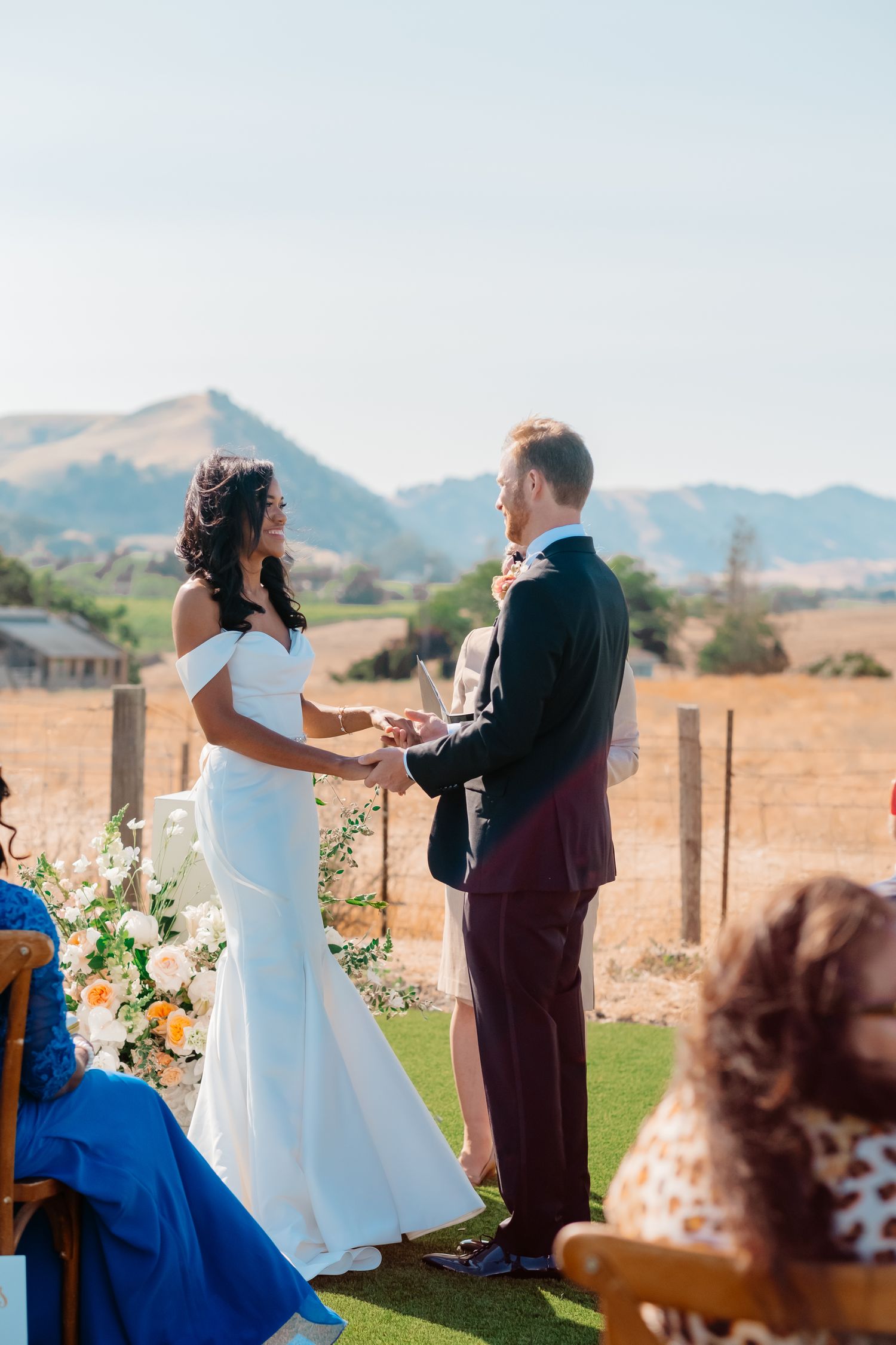 Bride and groom exchange vows outdoors with scenic rolling hills backdrop at a sunny California wedding ceremony.