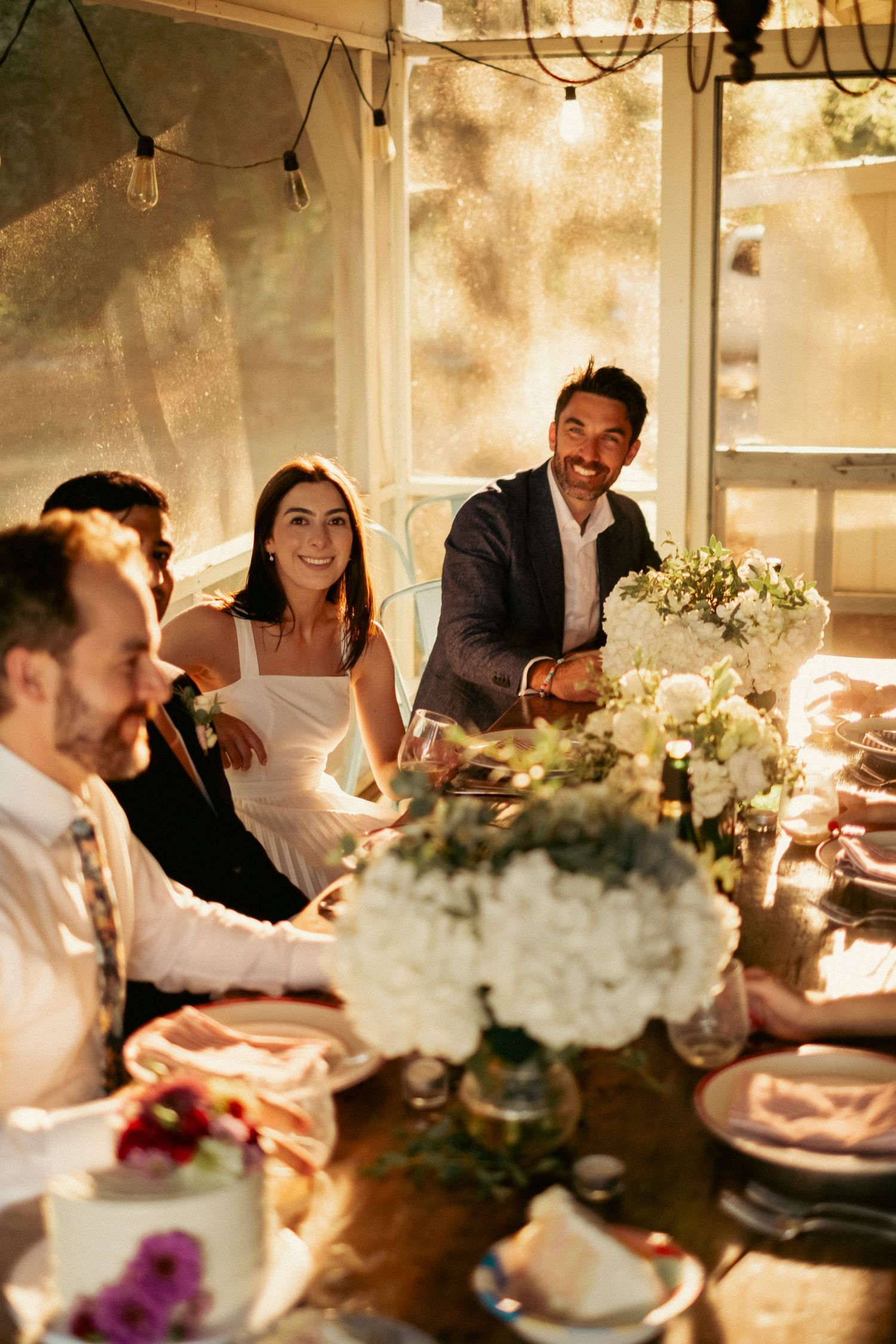 Bride and groom laughing with guests at warmly lit intimate wedding reception dinner table.