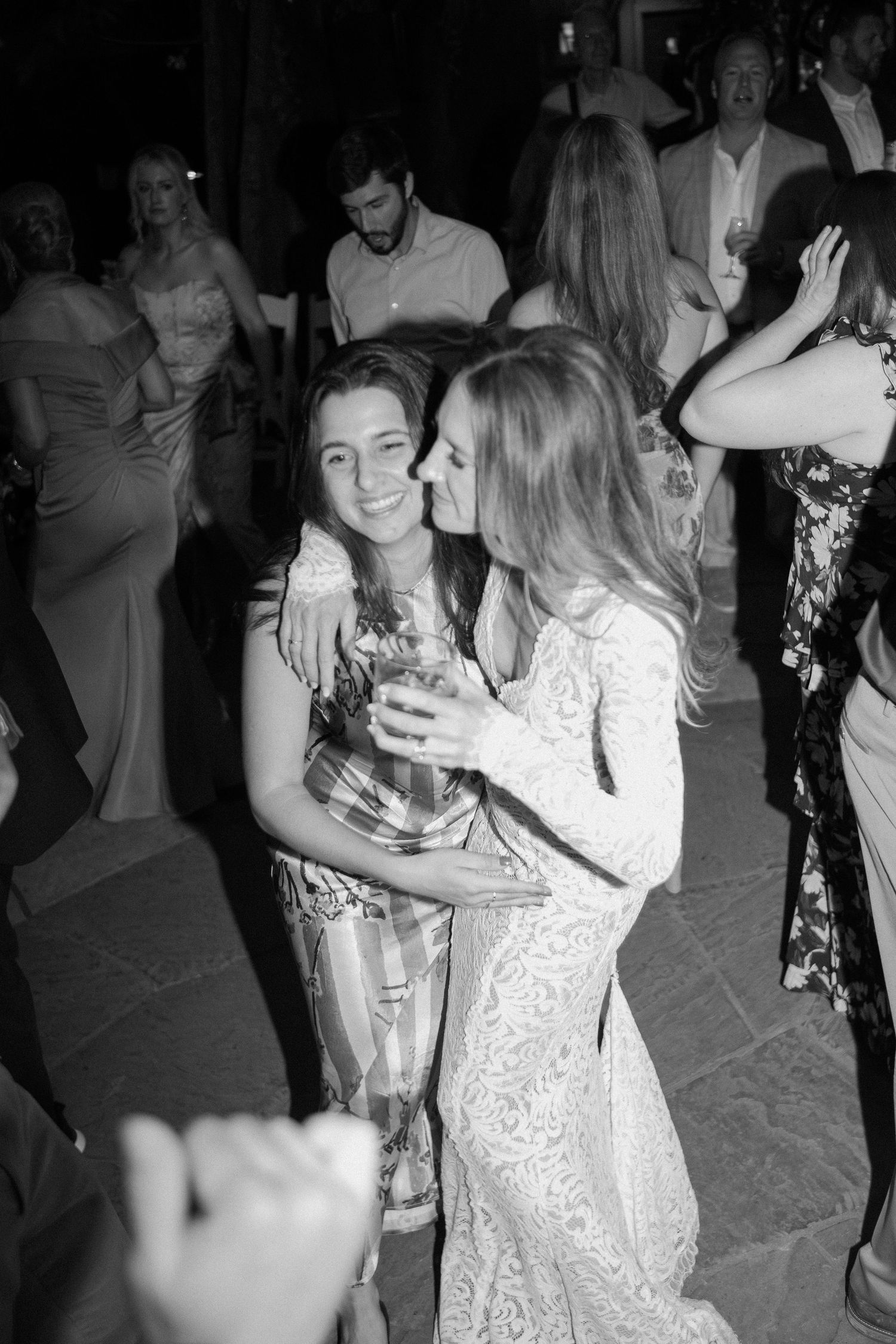 Black and white photo of bride in lace gown kissing guest on cheek at reception.