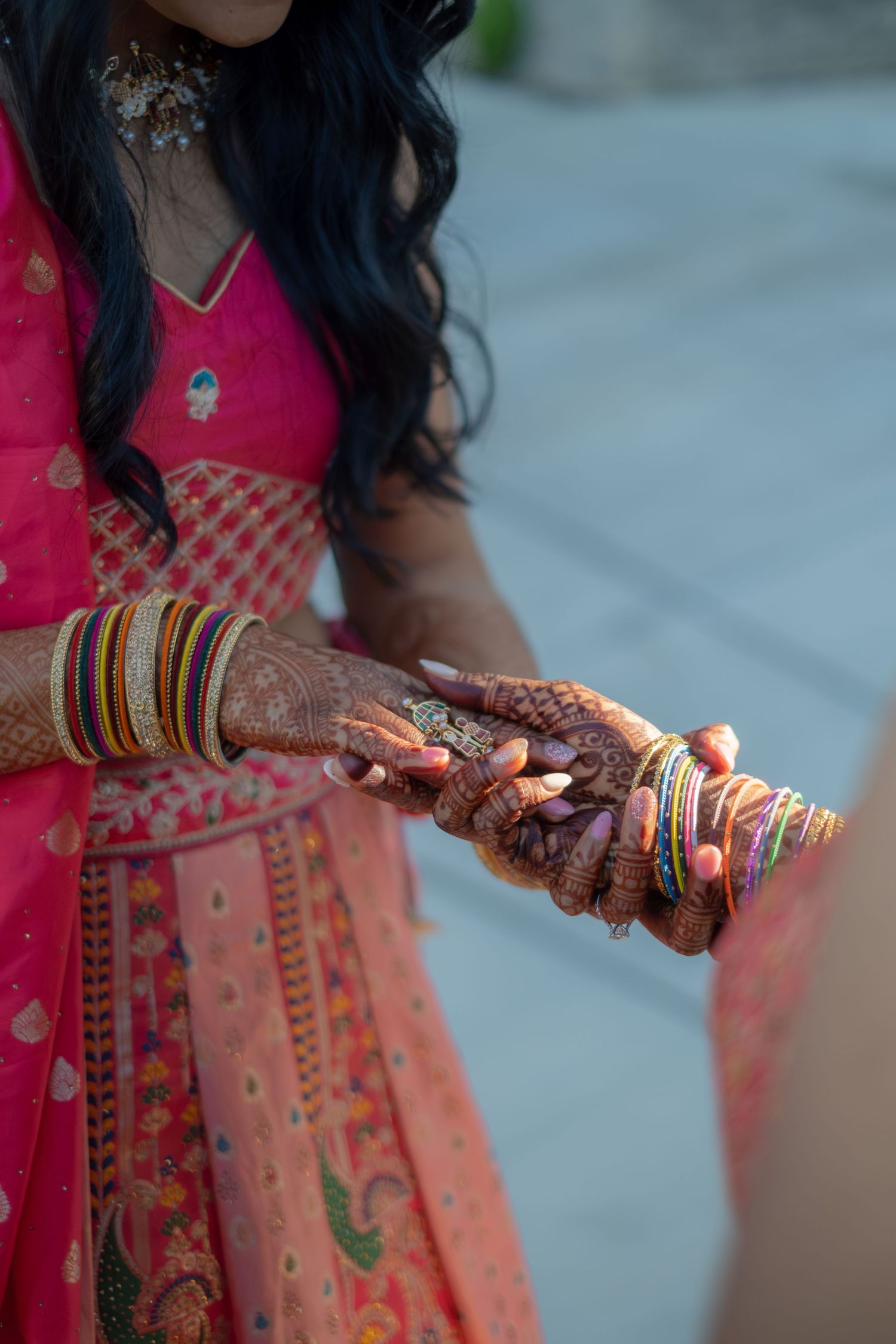 Indian bride in pink lehenga with intricate mehndi henna hands and colorful bangles holding hands at wedding ceremony.