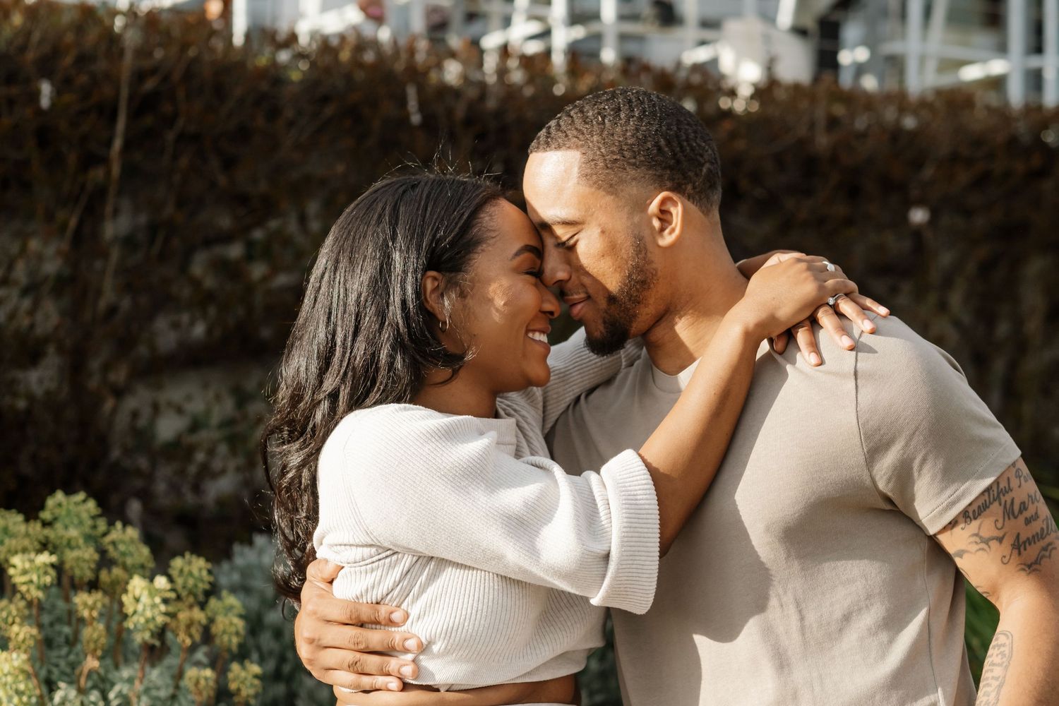 A loving Black couple shares an intimate moment, nearly kissing while embracing outdoors near lush greenery.