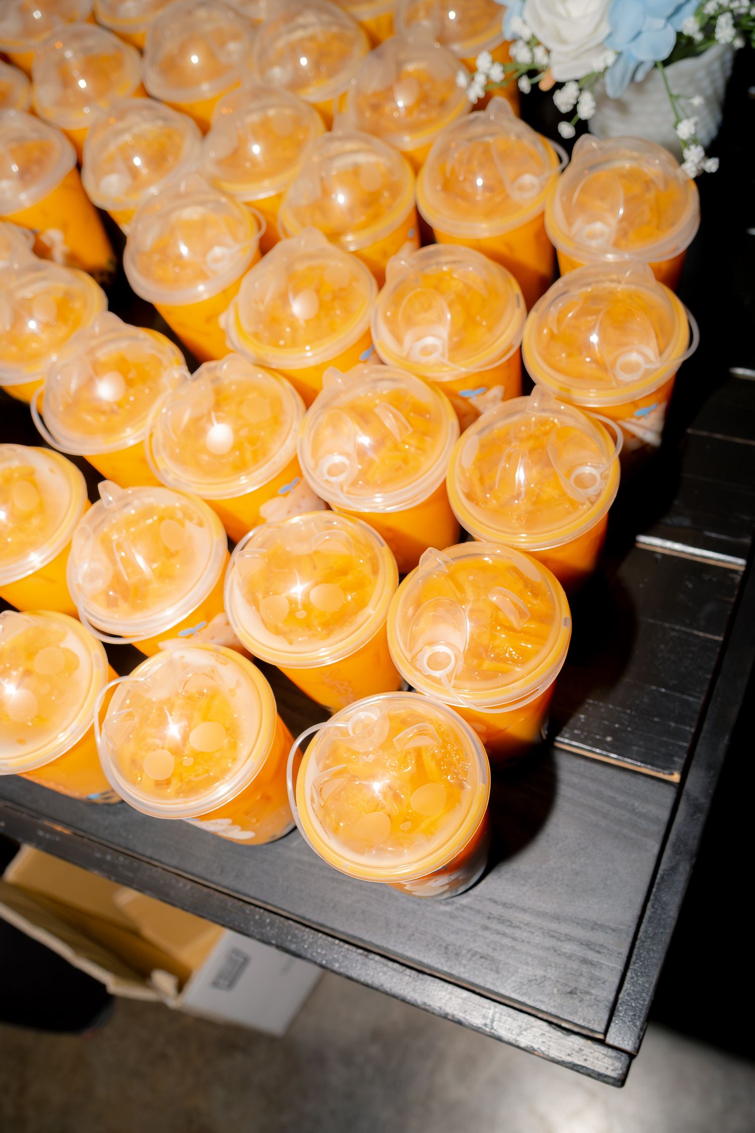Rows of orange mango drinks in clear plastic cups arranged on black tray as wedding reception refreshments.