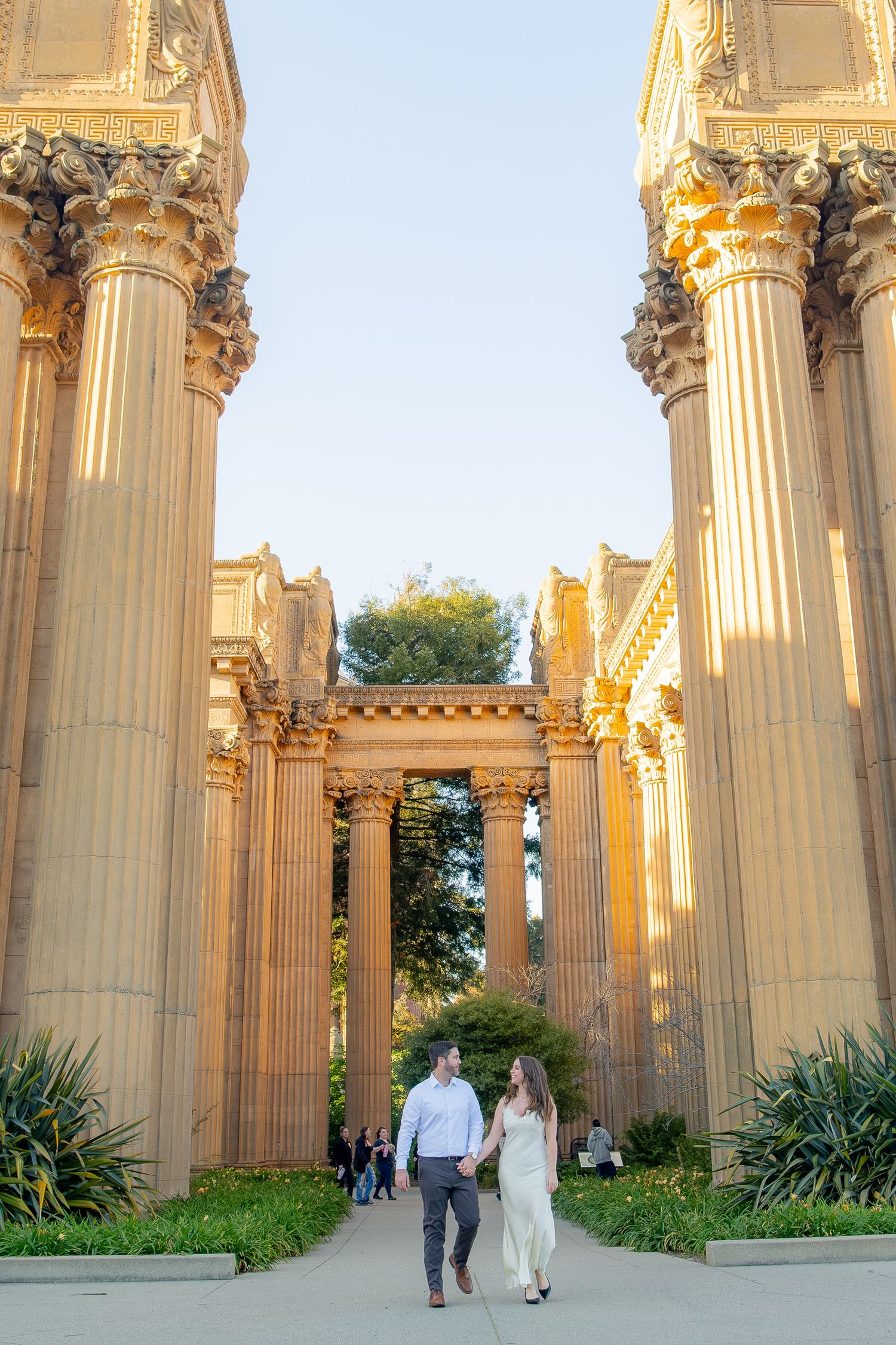Couple holding hands walking between grand Roman columns at the Palace of Fine Arts in San Francisco.