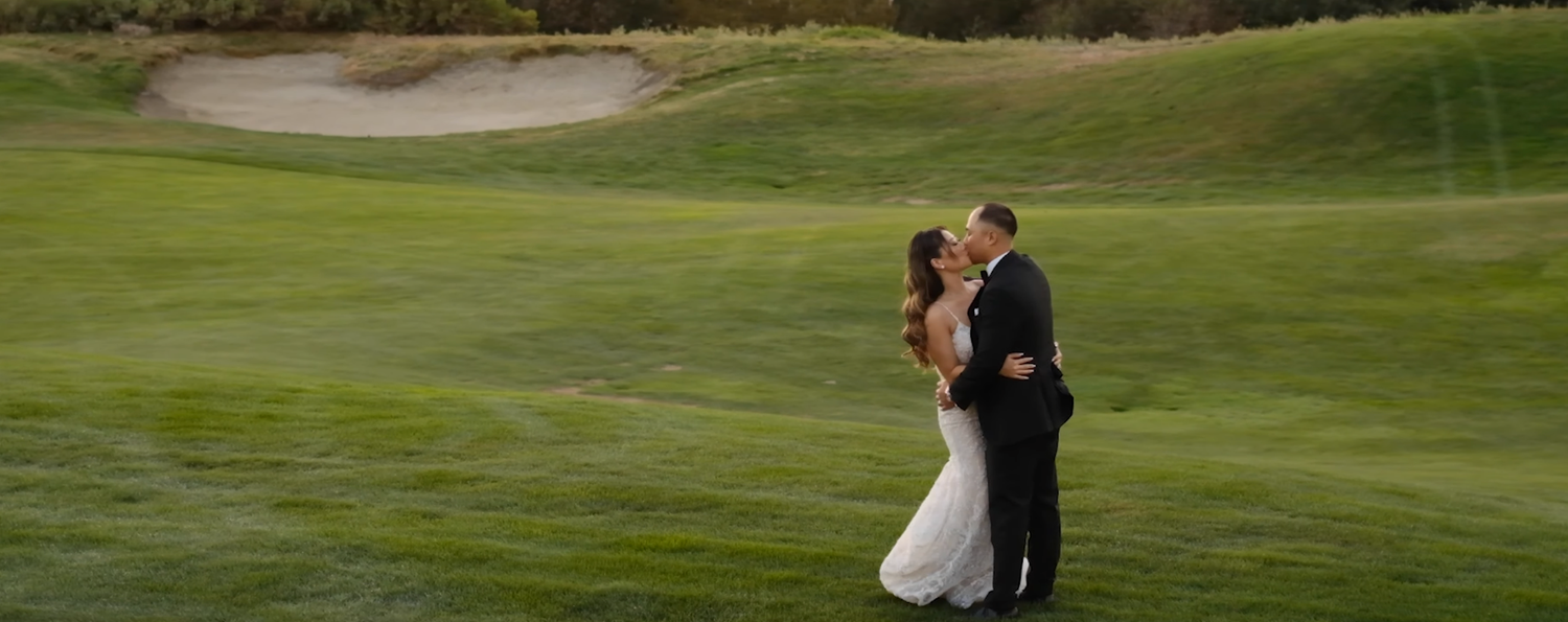 Romantic bride and groom sharing a kiss on a lush green golf course with rolling hills in the background.