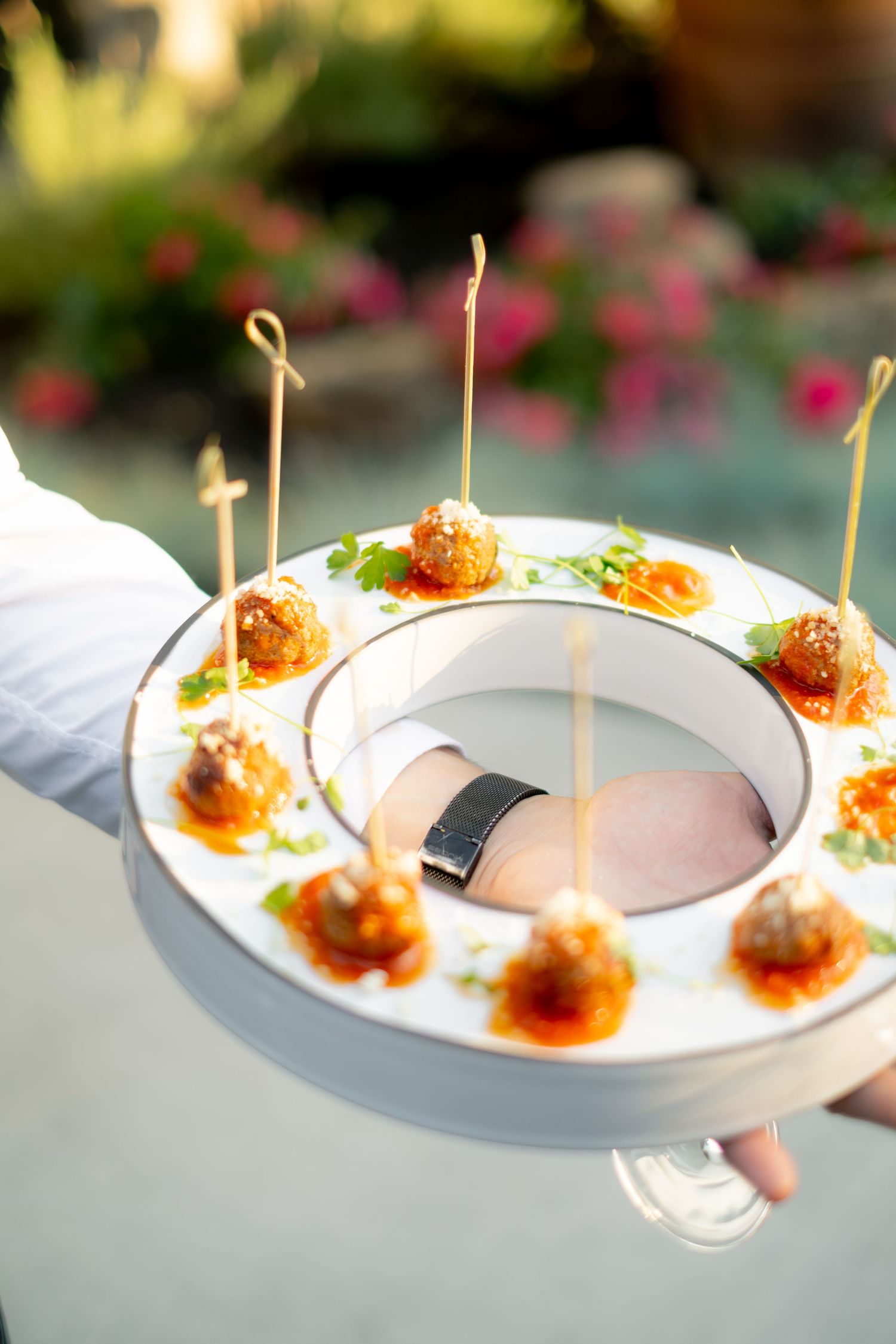 Catering server presenting elegant round tray of fried appetizer bites with toothpicks and herb garnish at wedding.