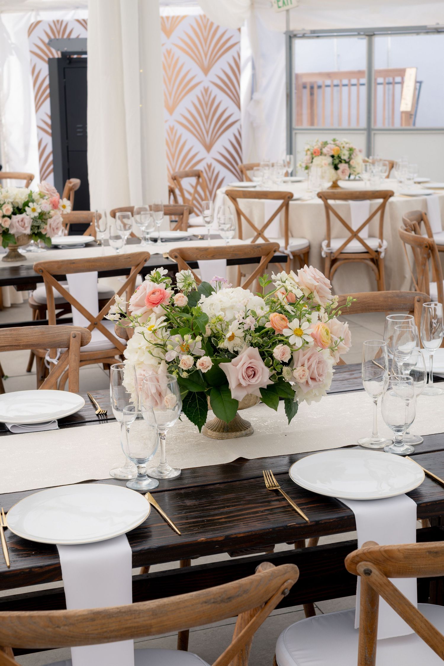 Elegant wedding reception tables with blush floral centerpieces, white plates, and gold cutlery.