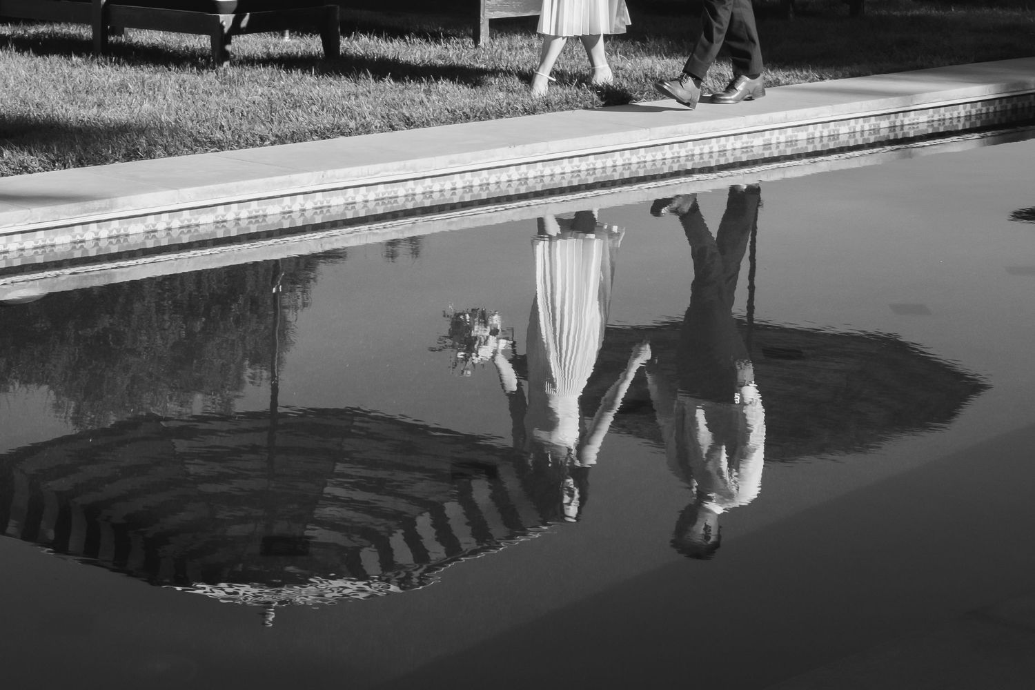 Black and white reflection of bride and groom in a still pool at their wedding.