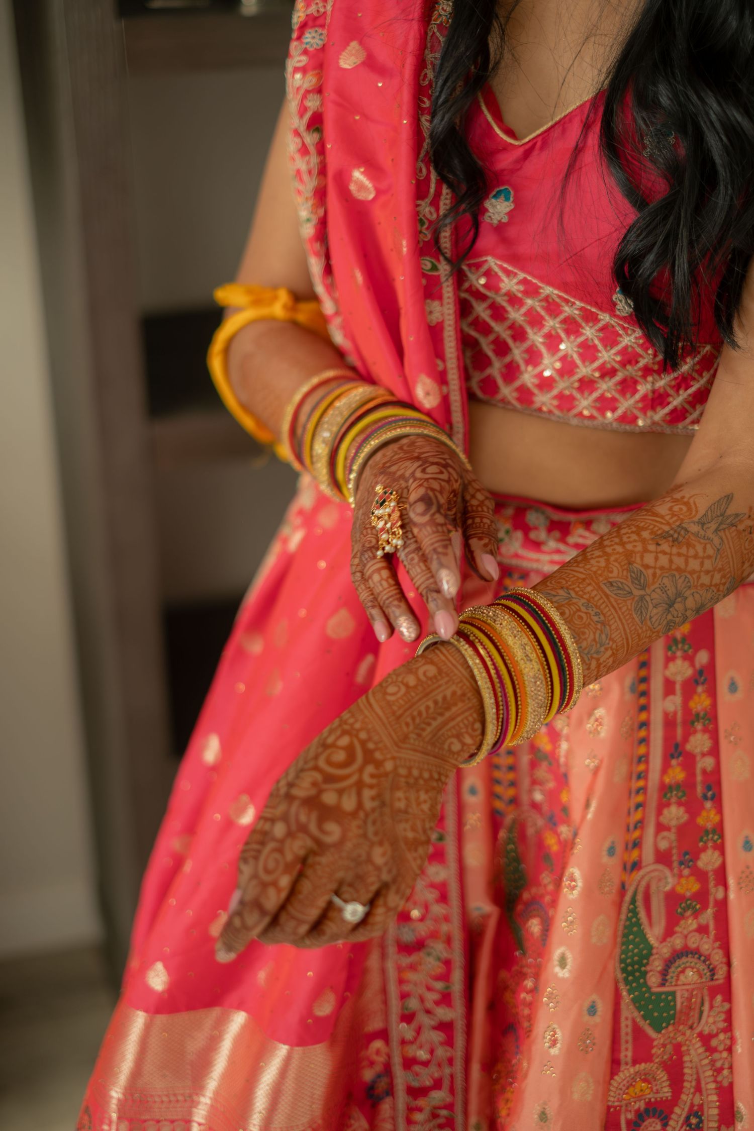 Close-up of Indian bride's hands with intricate henna mehndi designs and gold bangles on pink lehenga.