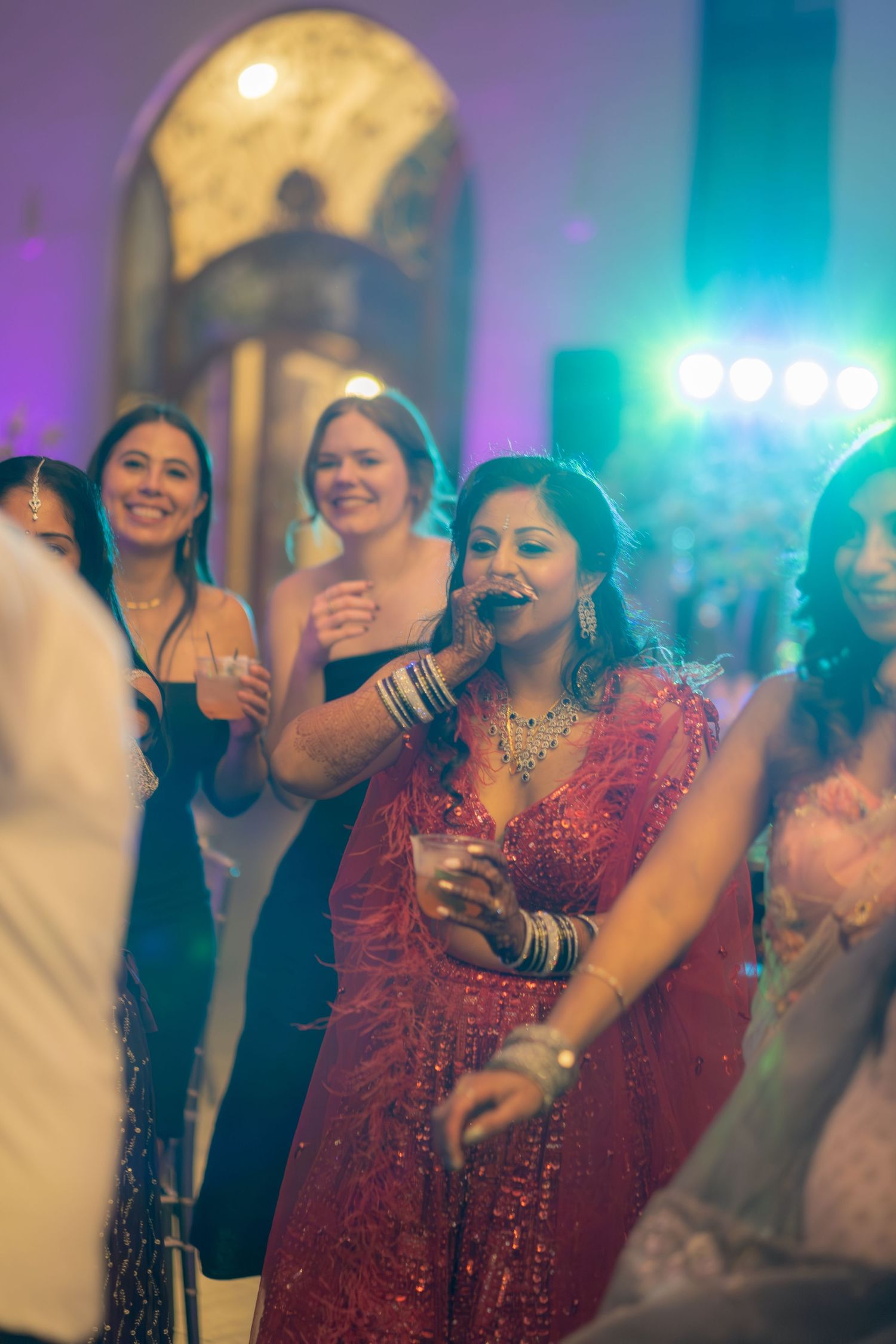 Woman in sparkling red saree enjoys lively Indian wedding reception dance floor celebration.