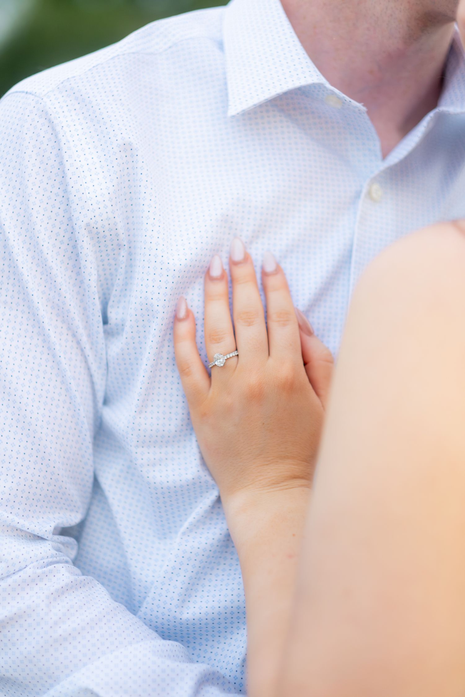 Close-up of woman's hand with engagement ring resting on man's chest.