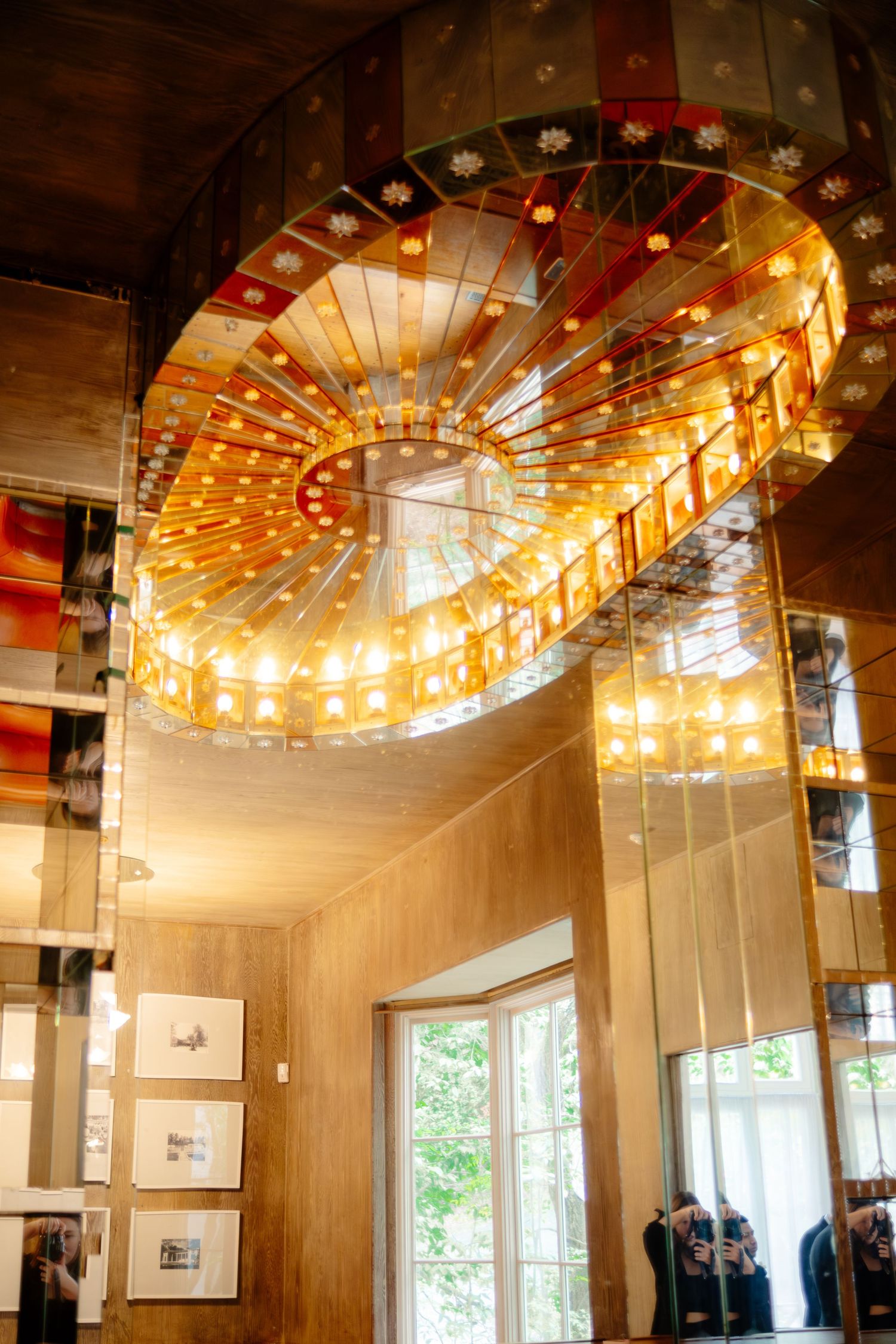 Ornate spiral chandelier with warm amber lights and floral details illuminates a modern interior with mirrored walls.