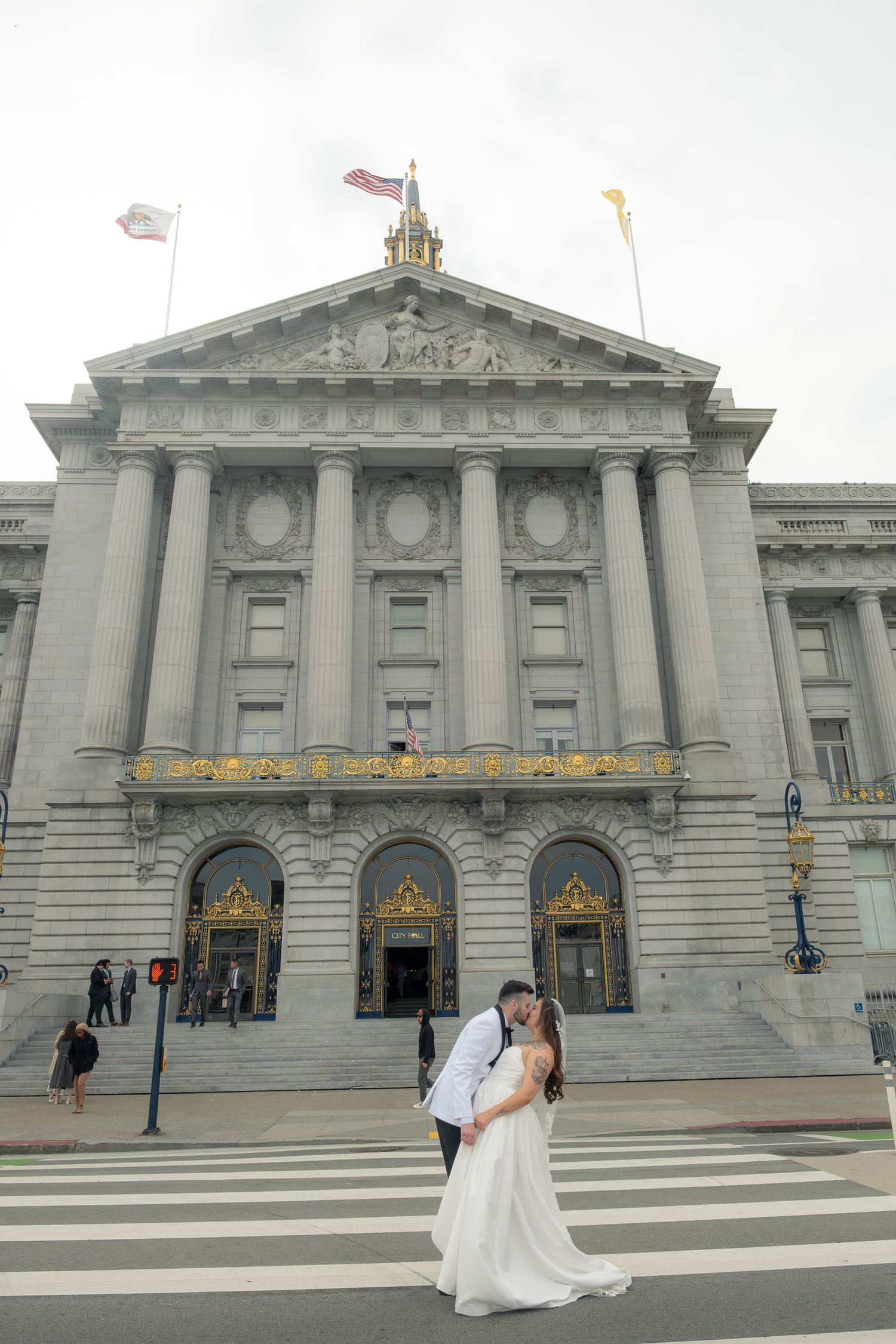 Bride and groom kissing on crosswalk in front of San Francisco City Hall on their wedding day.