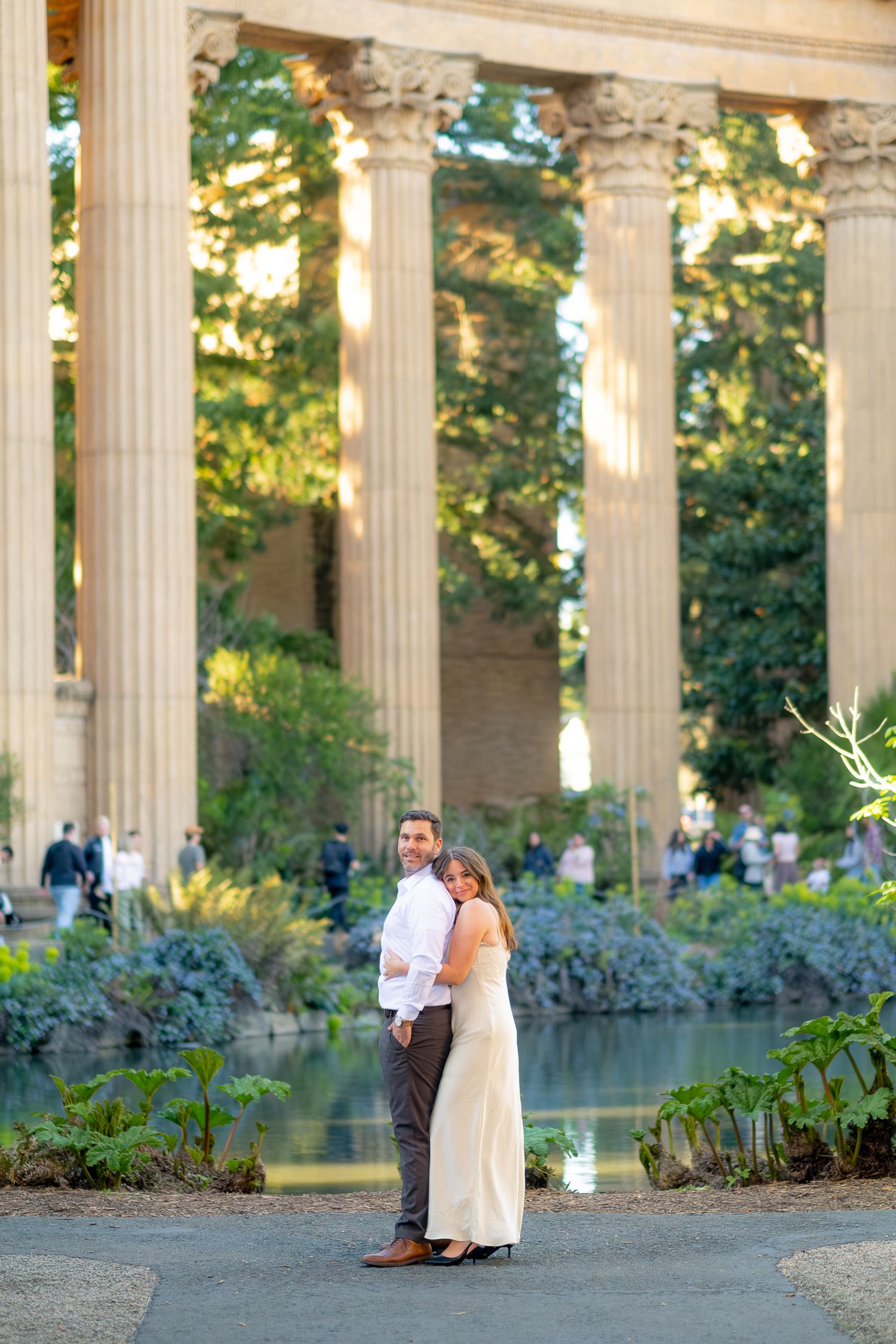 Couple posing together in front of grand classical columns and lagoon at Palace of Fine Arts SF.