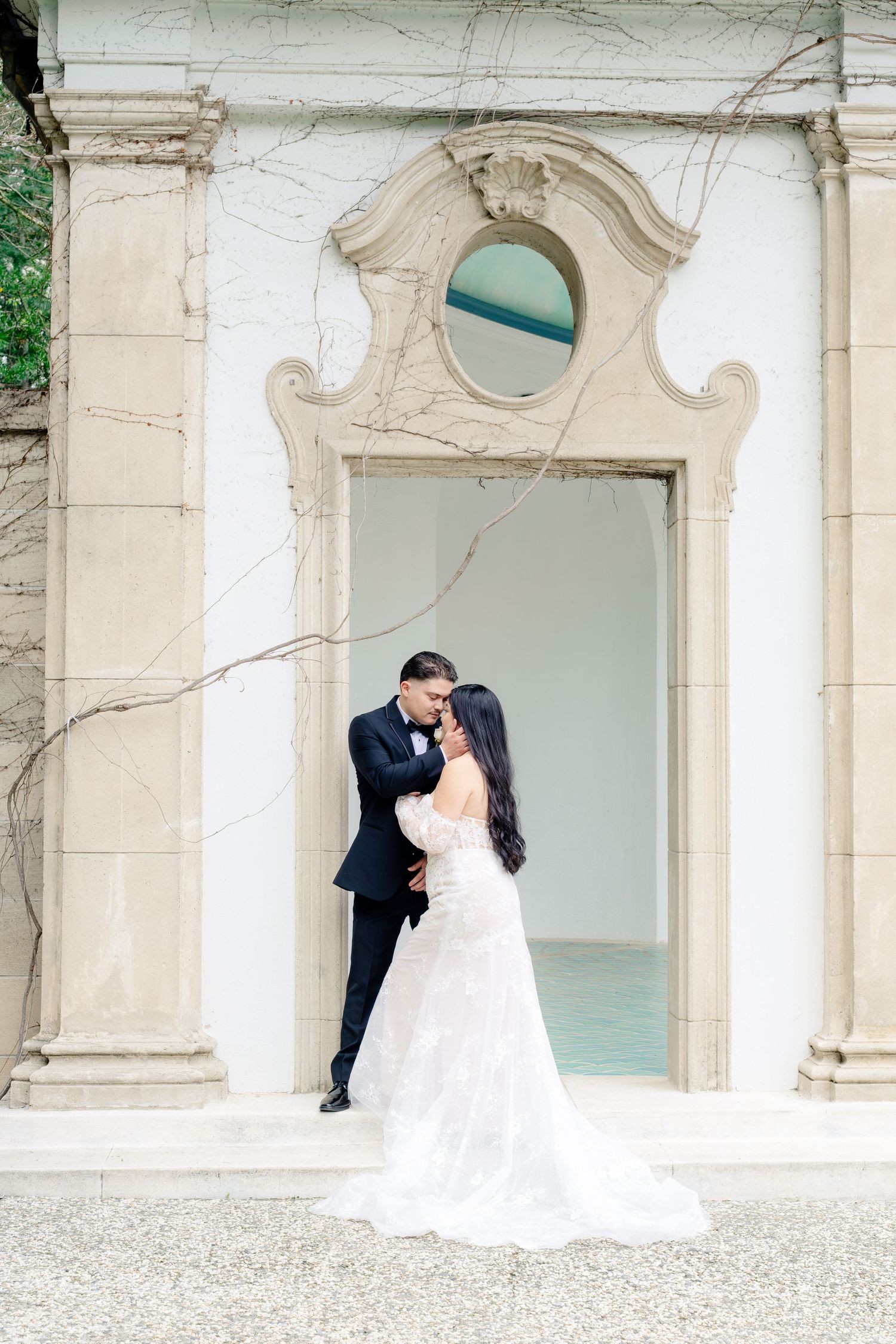 Bride and groom sharing romantic embrace before ornate architectural doorway at wedding photo session.