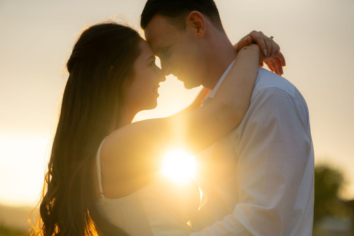 Romantic couple embracing at sunset with warm golden backlight during outdoor engagement session.
