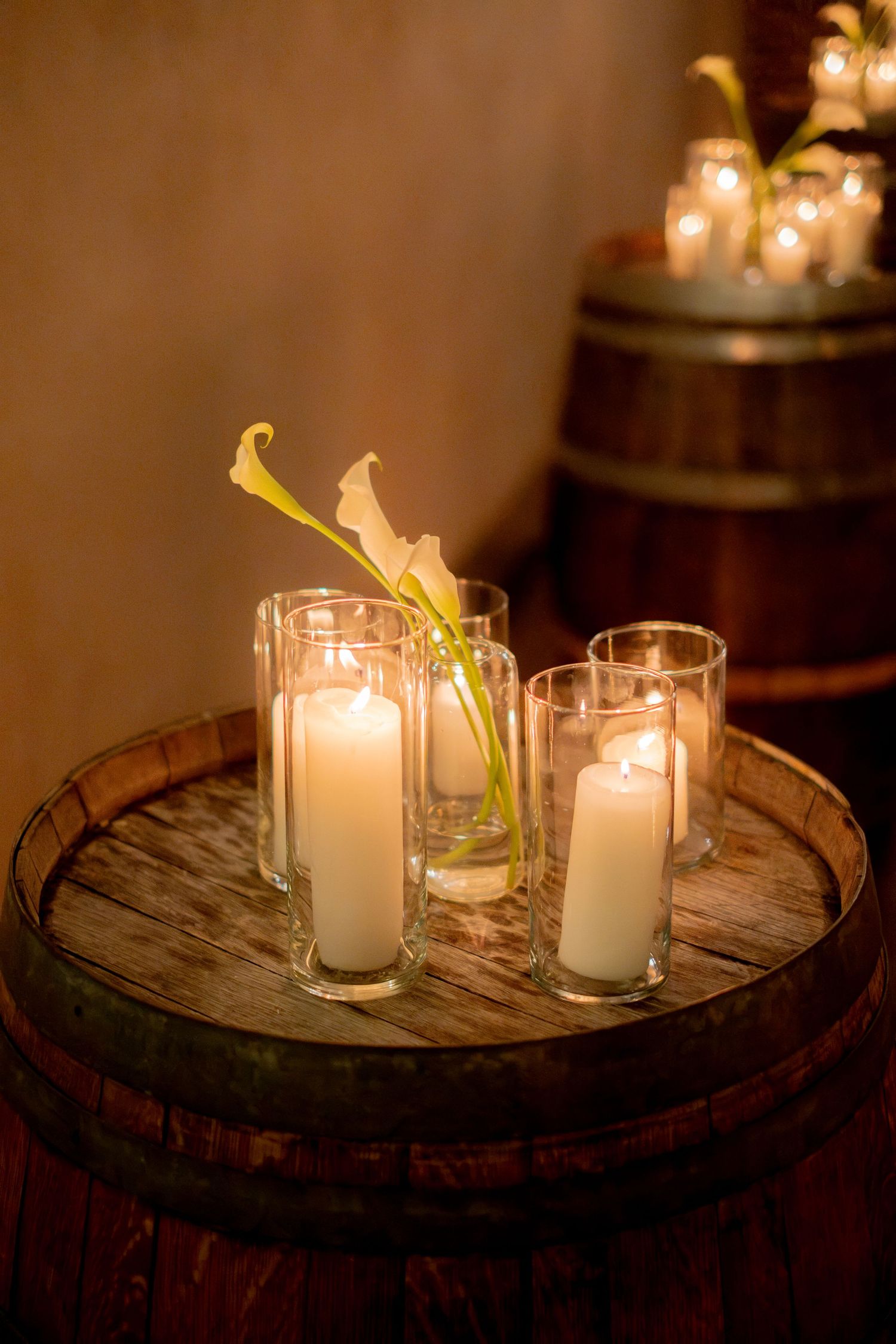 Romantic wedding decor with white pillar candles in glass holders atop a rustic wooden wine barrel.