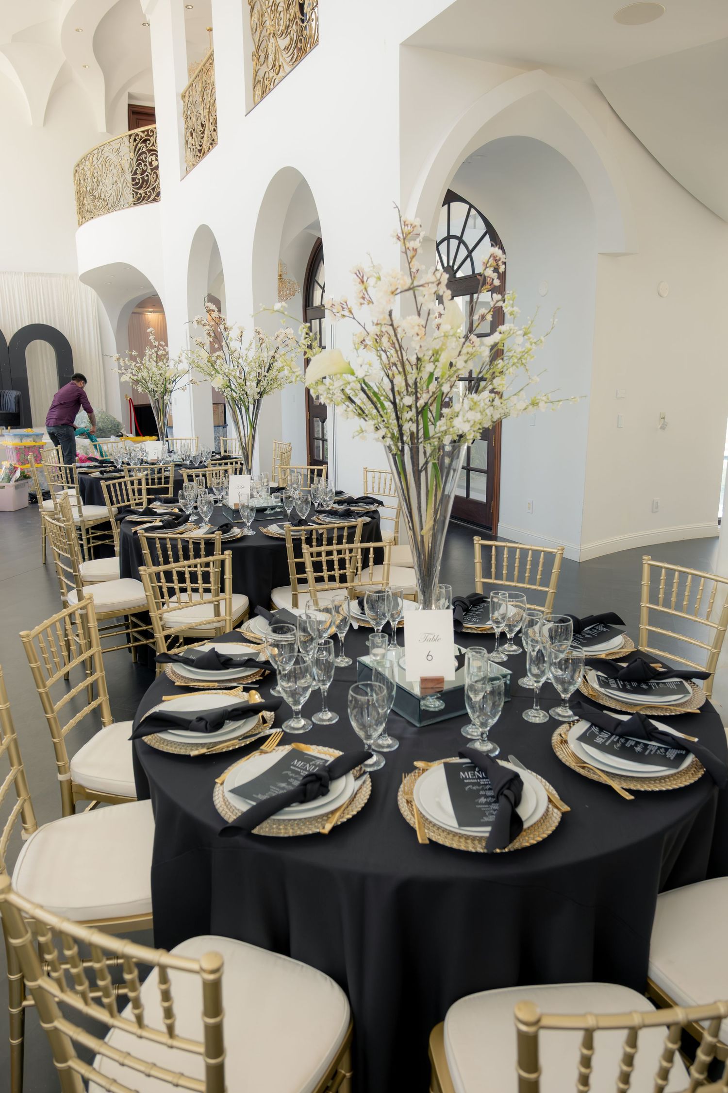 Elegant wedding reception tables with black linens, gold chiavari chairs, and white floral centerpieces.