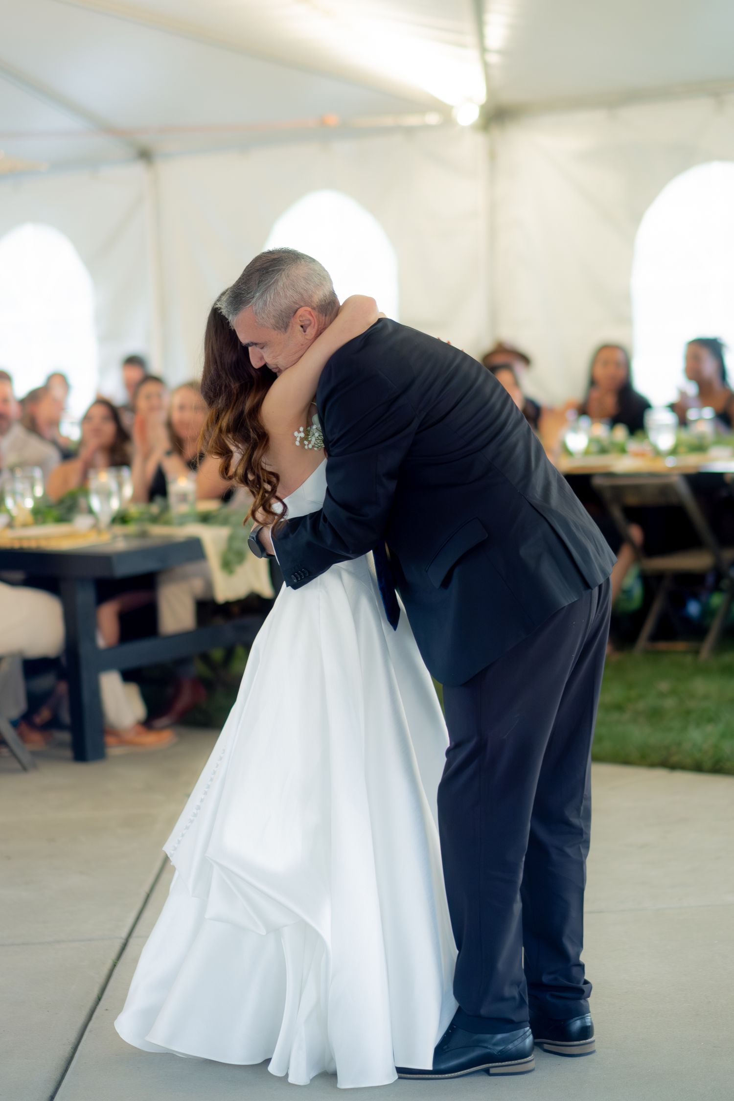 Bride and groom sharing an emotional first dance embrace under a white tent with wedding guests watching.