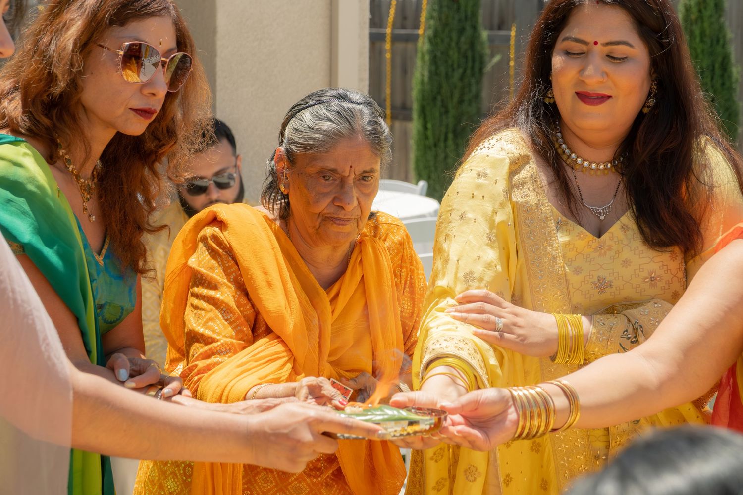 Women in colorful traditional Indian attire participate in a ceremonial ritual outdoors on a sunny day.
