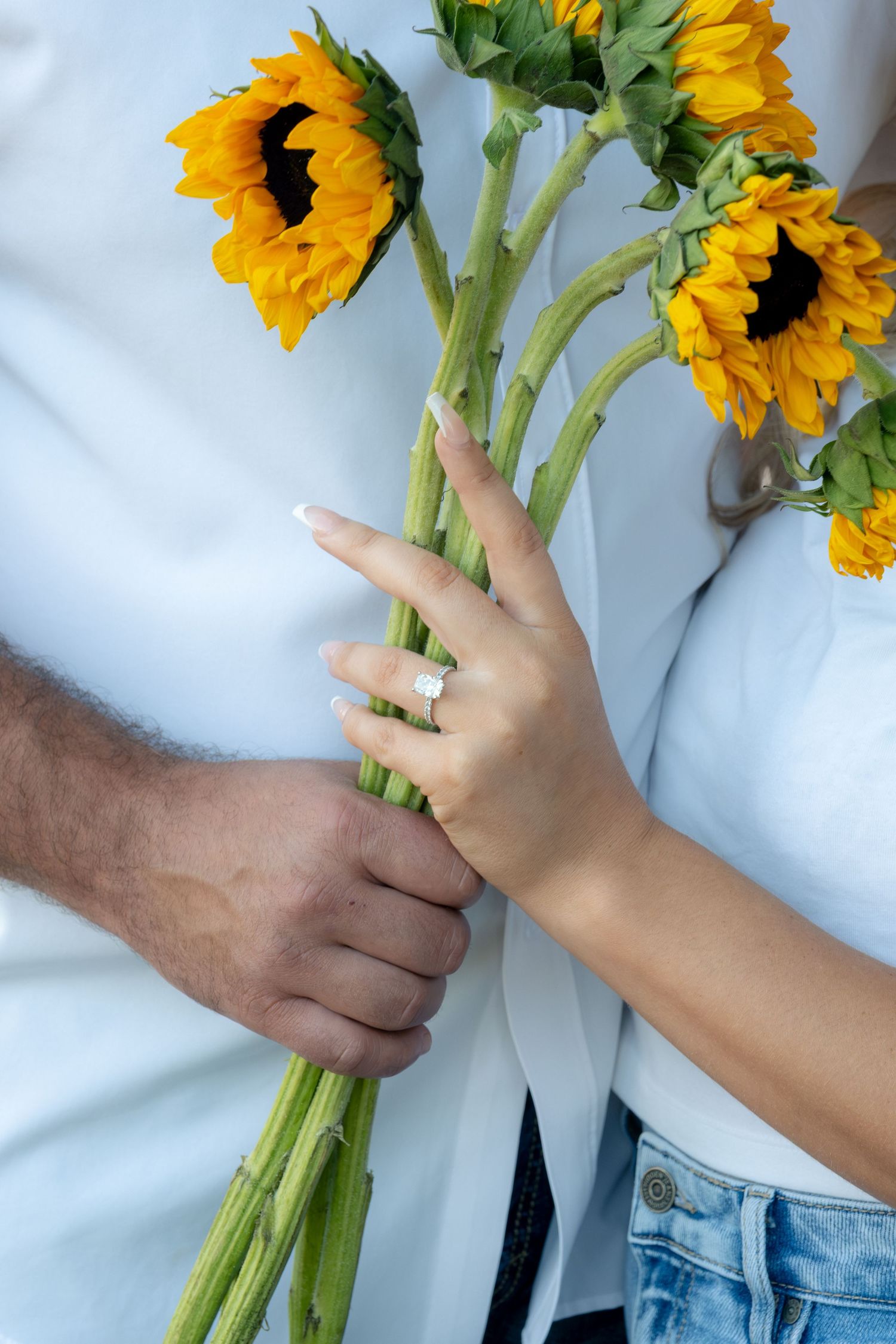 Close-up of engaged couple holding sunflowers with a sparkling diamond ring on woman's hand.