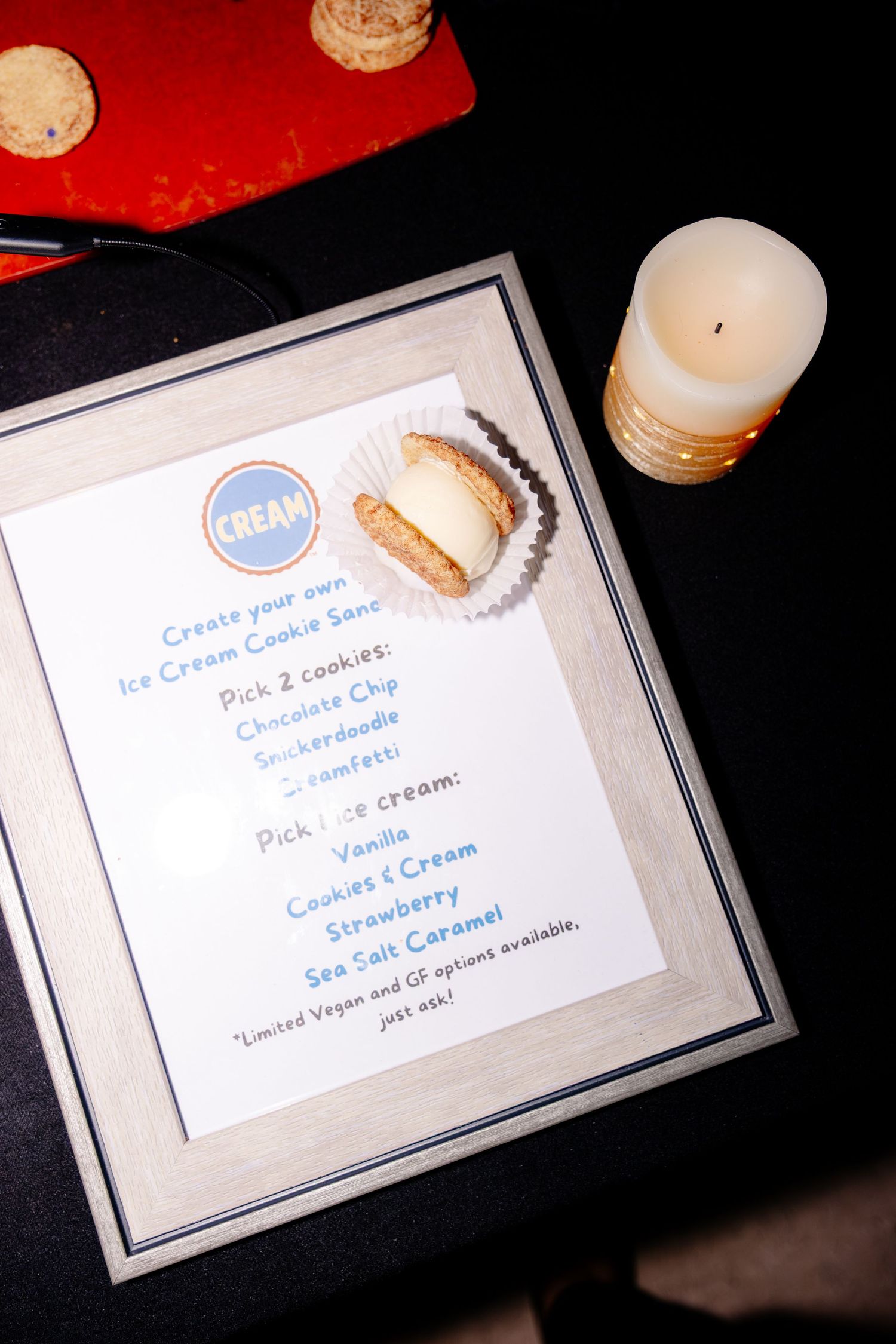 A framed CREAM ice cream cookie sandwich menu displayed beside a lit candle at a wedding reception dessert station.