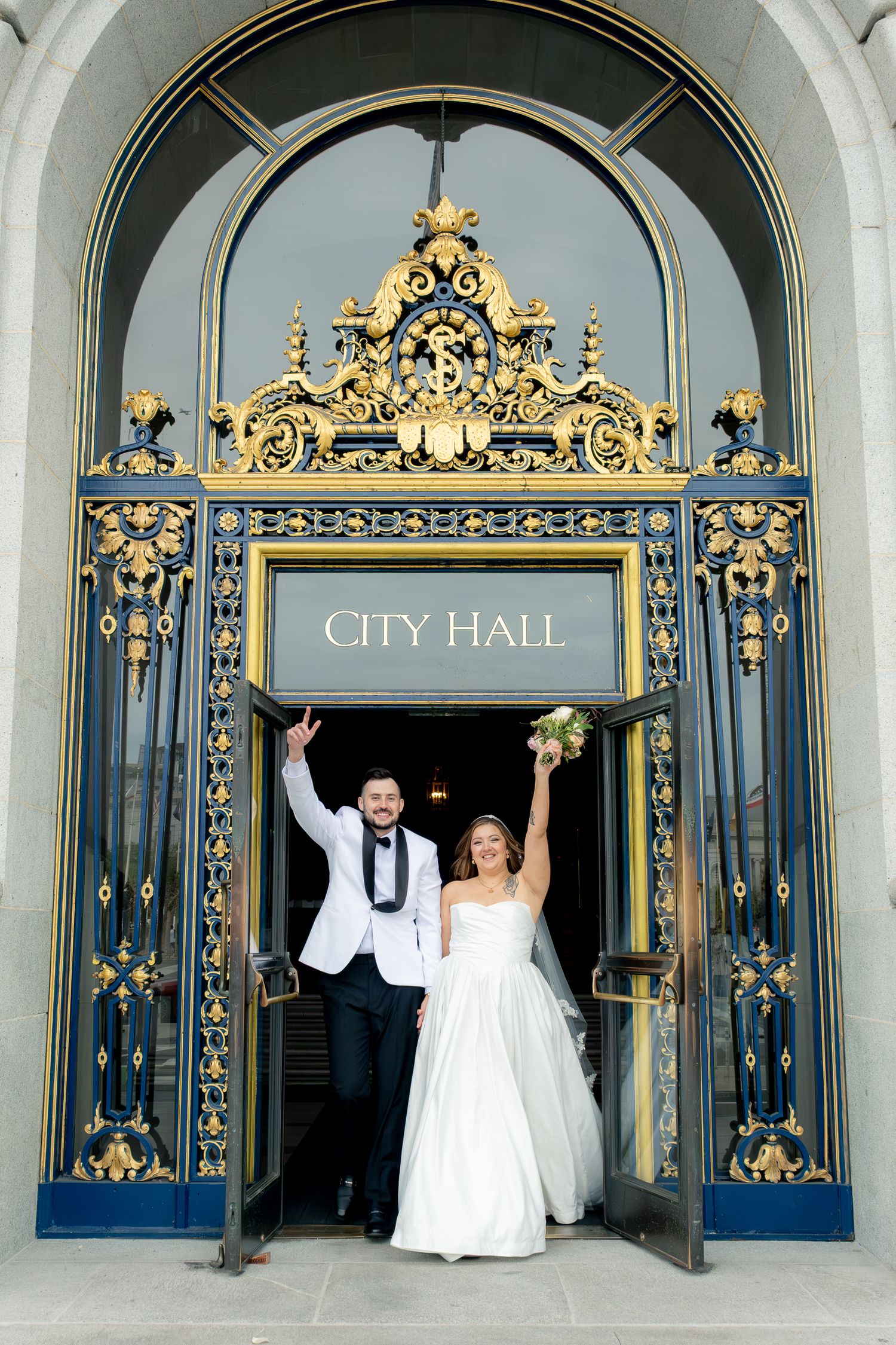 Jubilant newlyweds raise their arms in celebration exiting San Francisco City Hall's ornate gold doors.