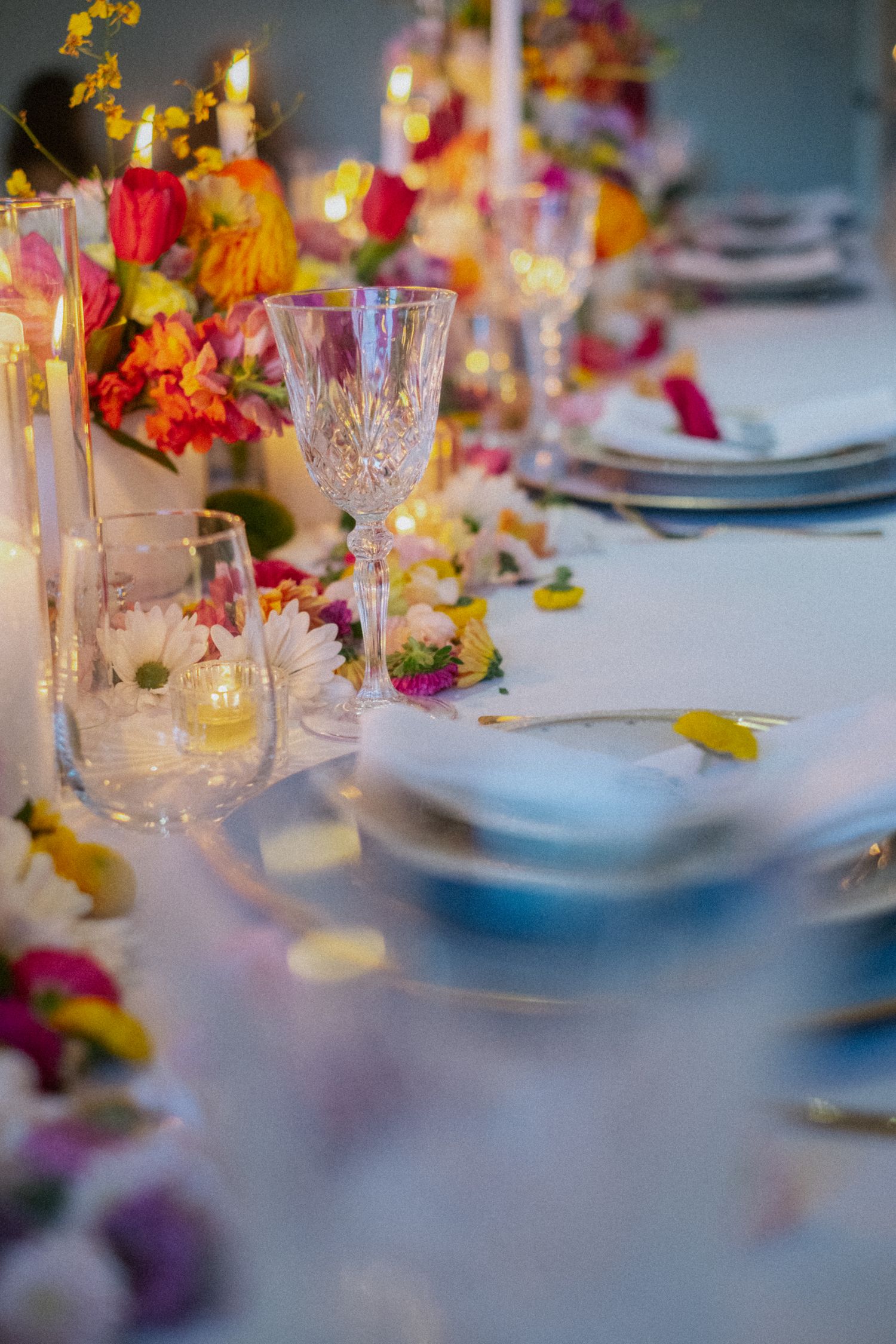 Elegant wedding reception table with colorful floral centerpieces, crystal glasses, and glowing candles.