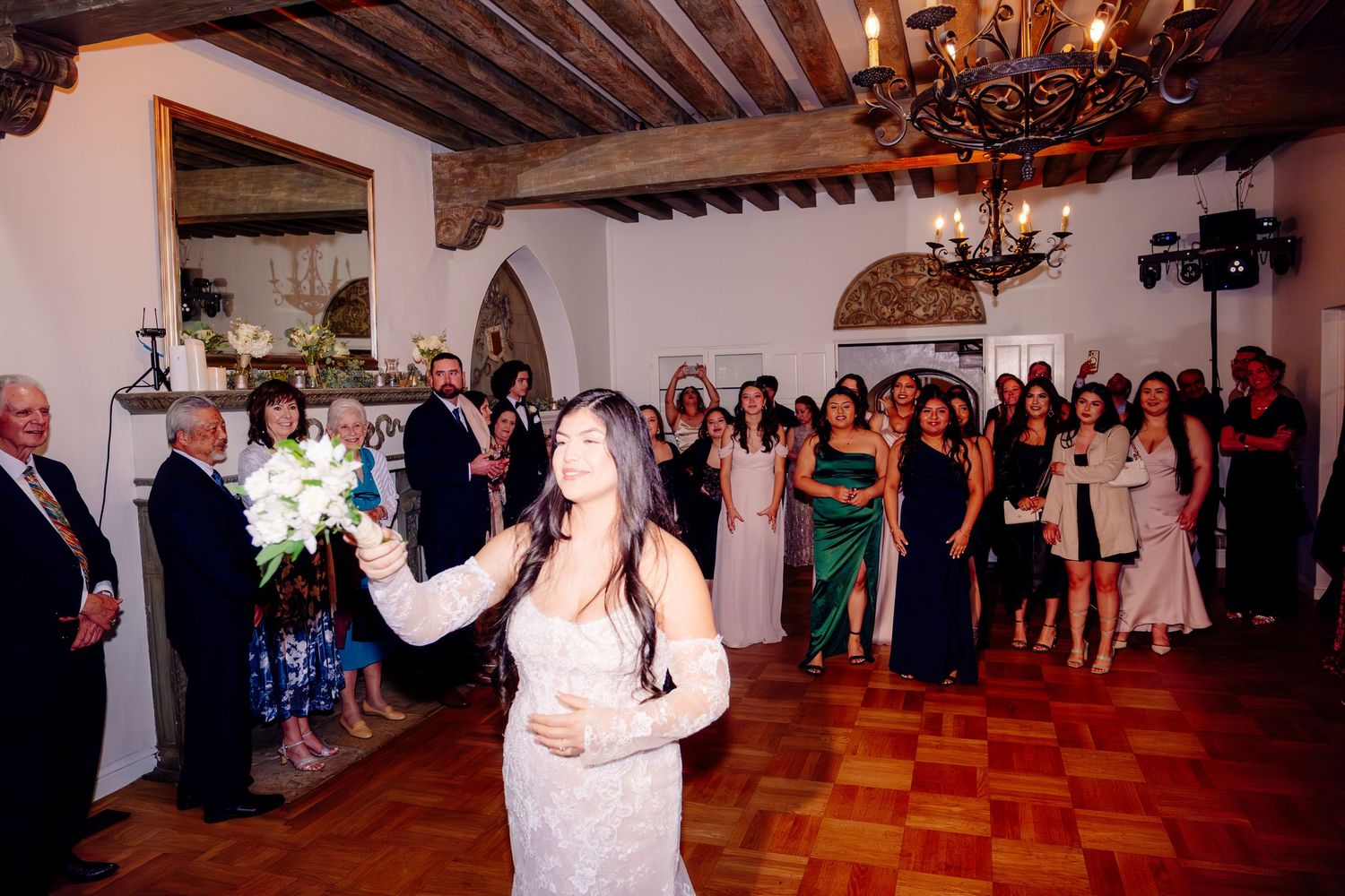 Bride tosses bouquet to excited crowd of female wedding guests during reception celebration.