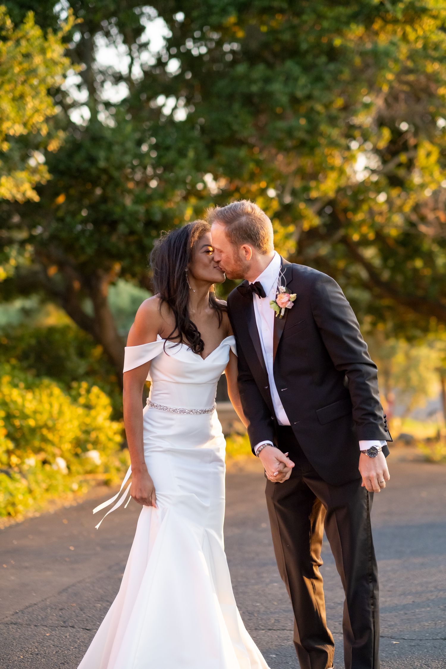 Bride and groom sharing a kiss on a tree-lined path at sunset wedding.