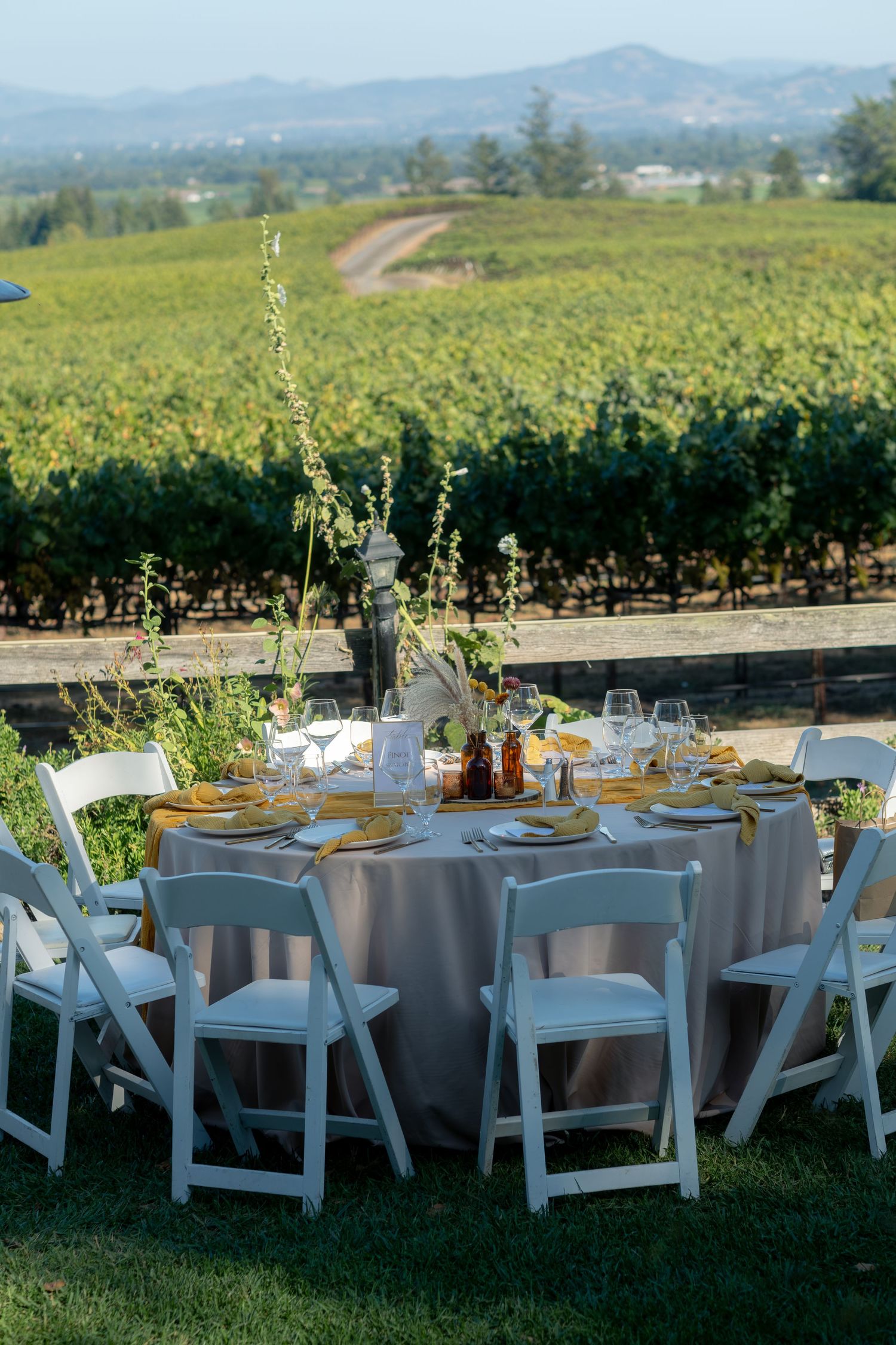 Elegant outdoor wedding reception table set with gold accents overlooking a scenic vineyard landscape.