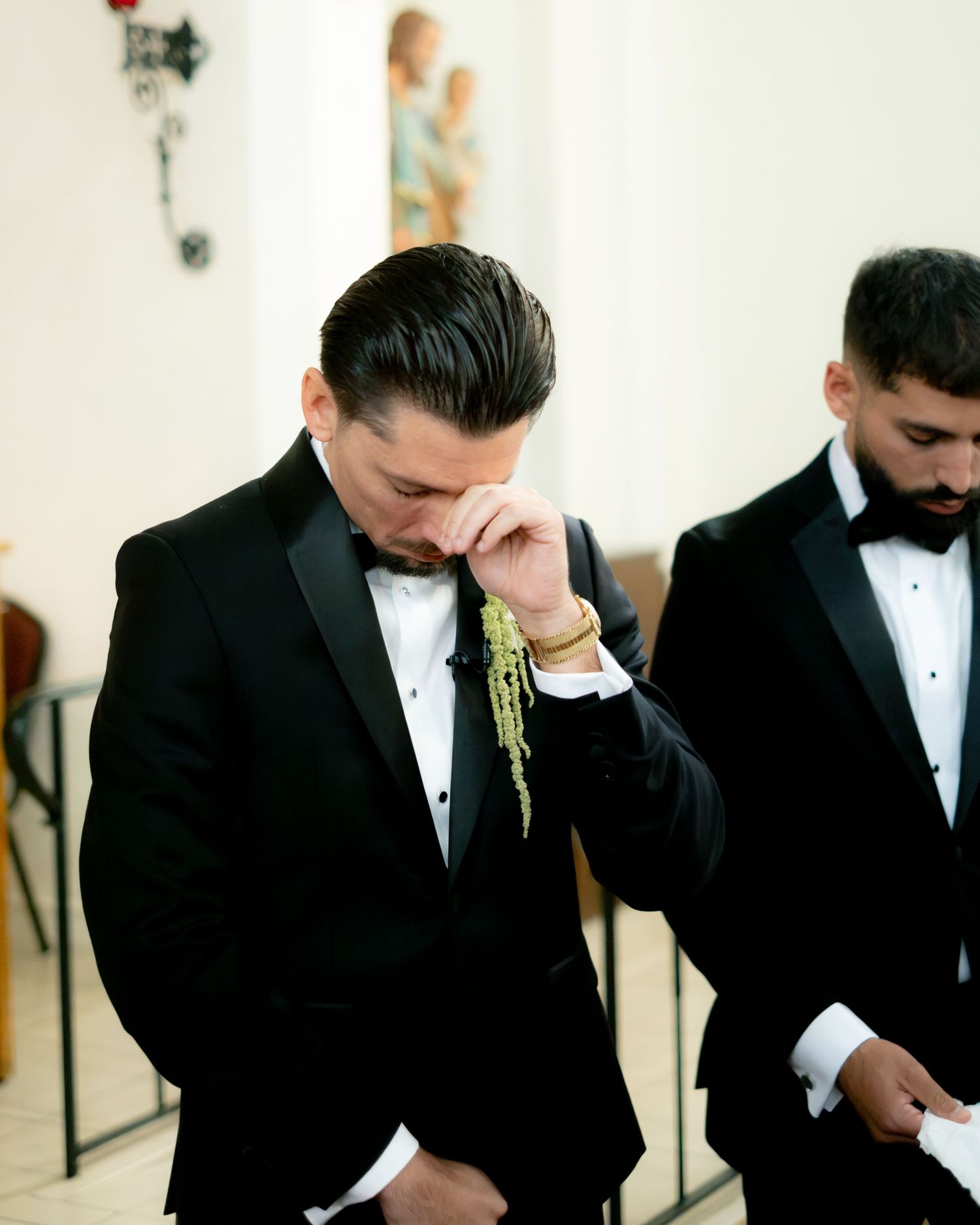 Emotional groom in black tuxedo wiping tears during wedding ceremony at church altar.