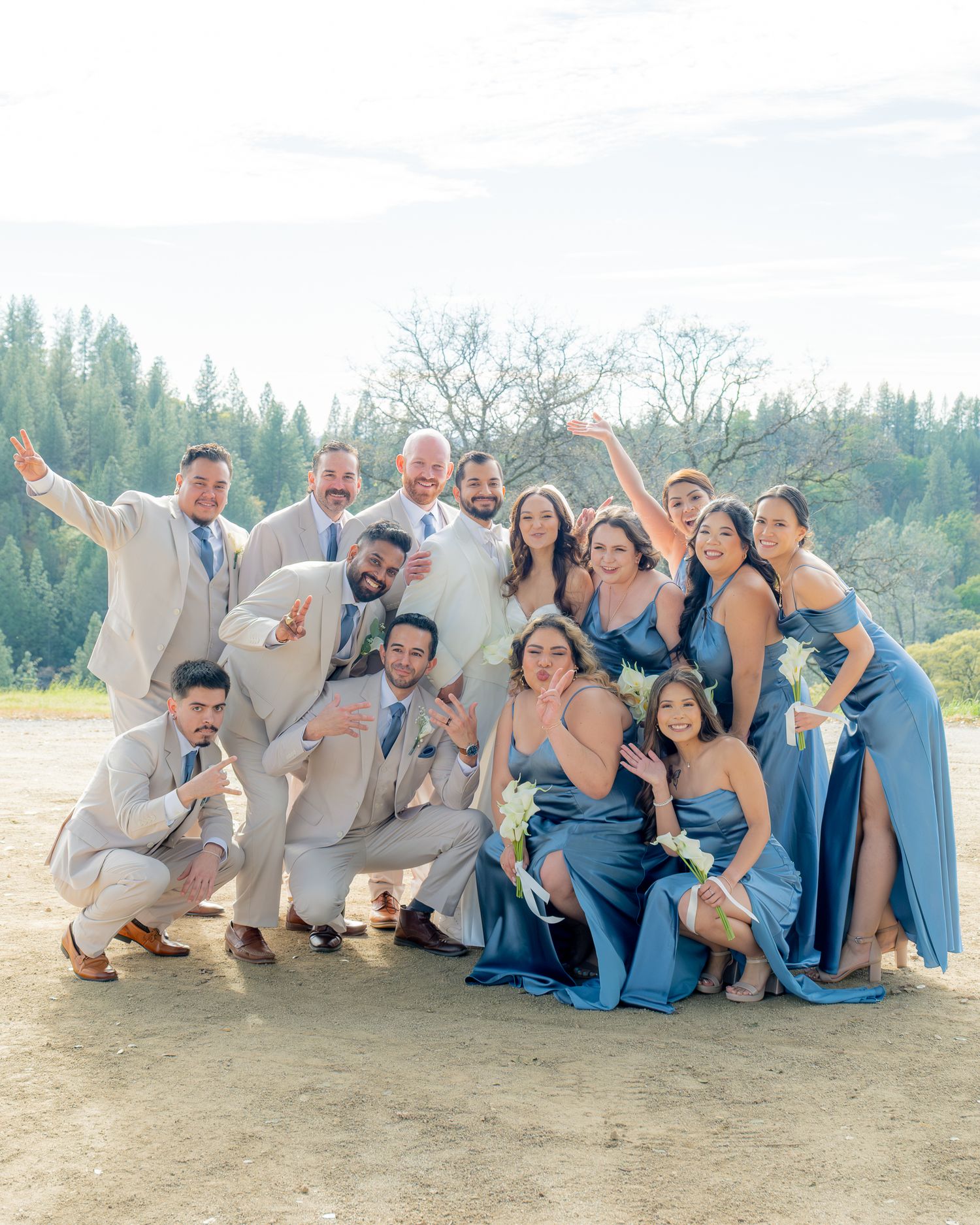 Wedding party poses outdoors with bridesmaids in blue dresses and groomsmen in tan suits.