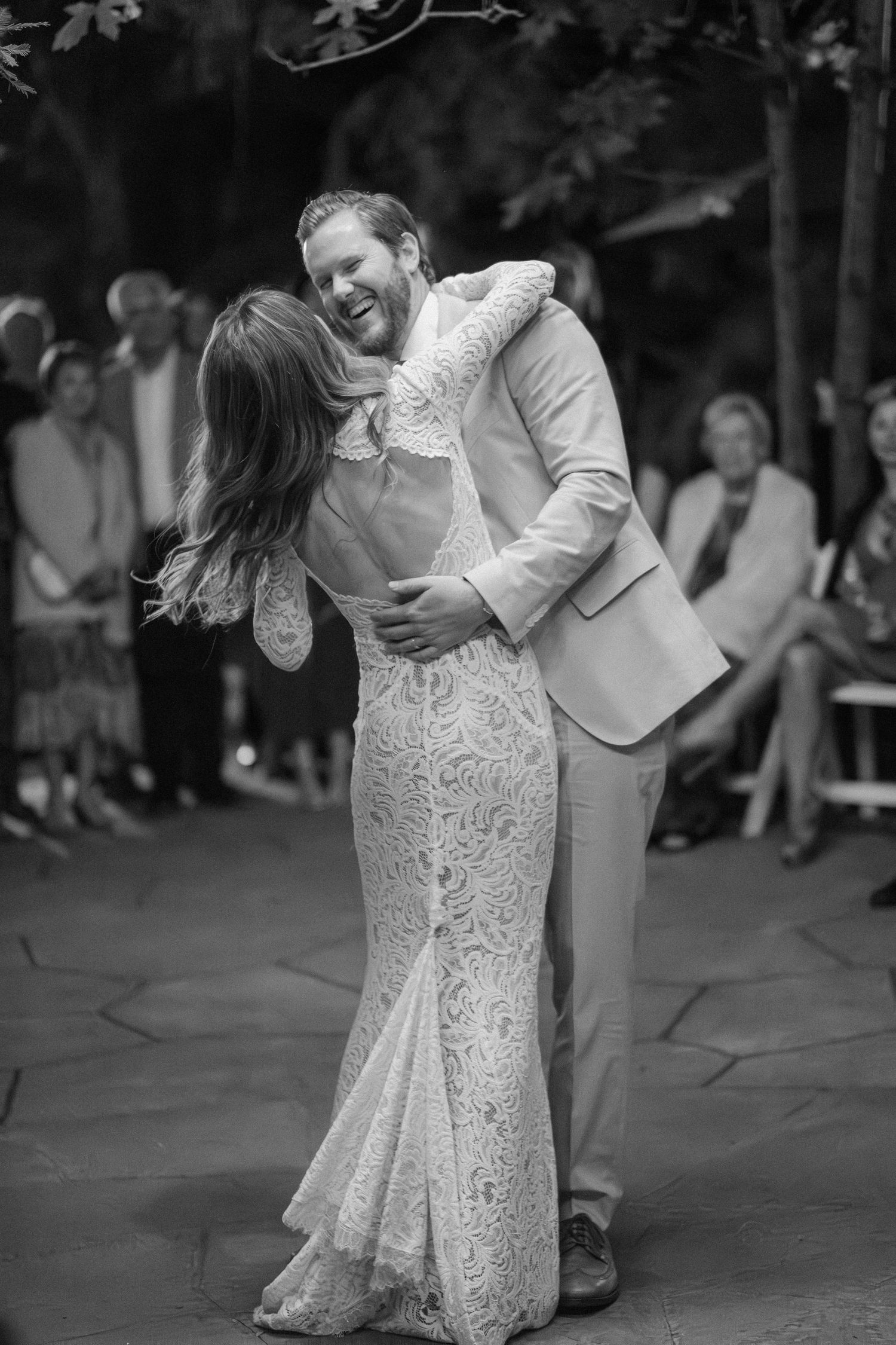 Black and white photo of bride and groom sharing joyful first dance at outdoor wedding reception.