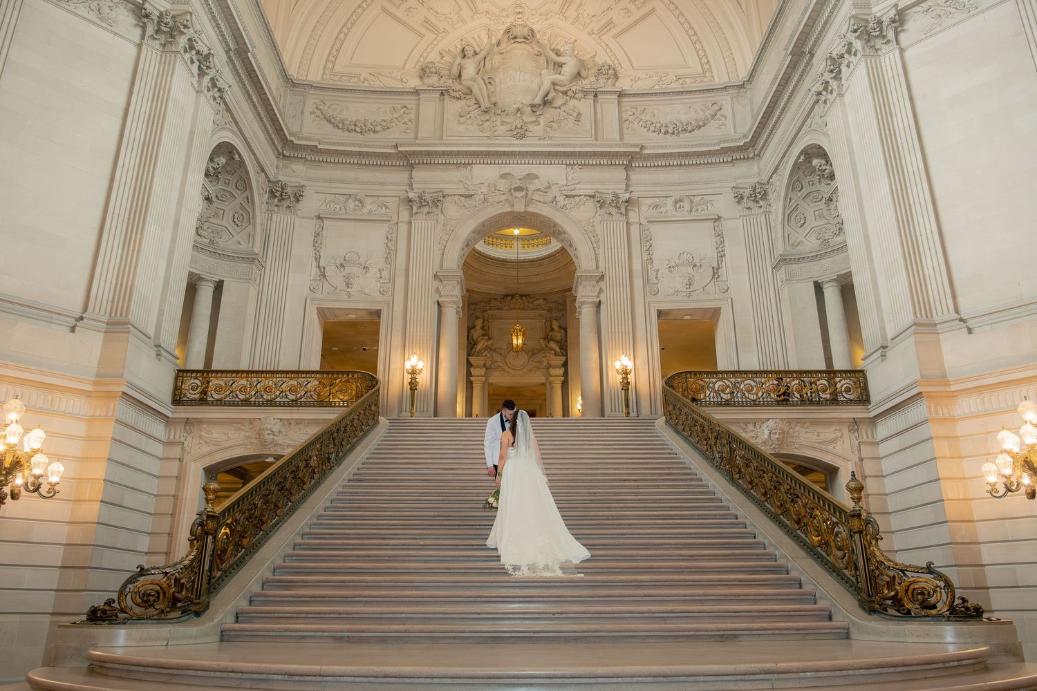 Bride and groom walking up grand staircase at San Francisco City Hall wedding ceremony.