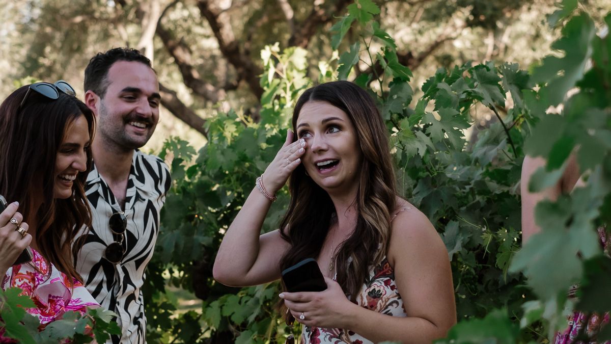 Joyful woman covering her mouth in surprise during a proposal moment in a vineyard.