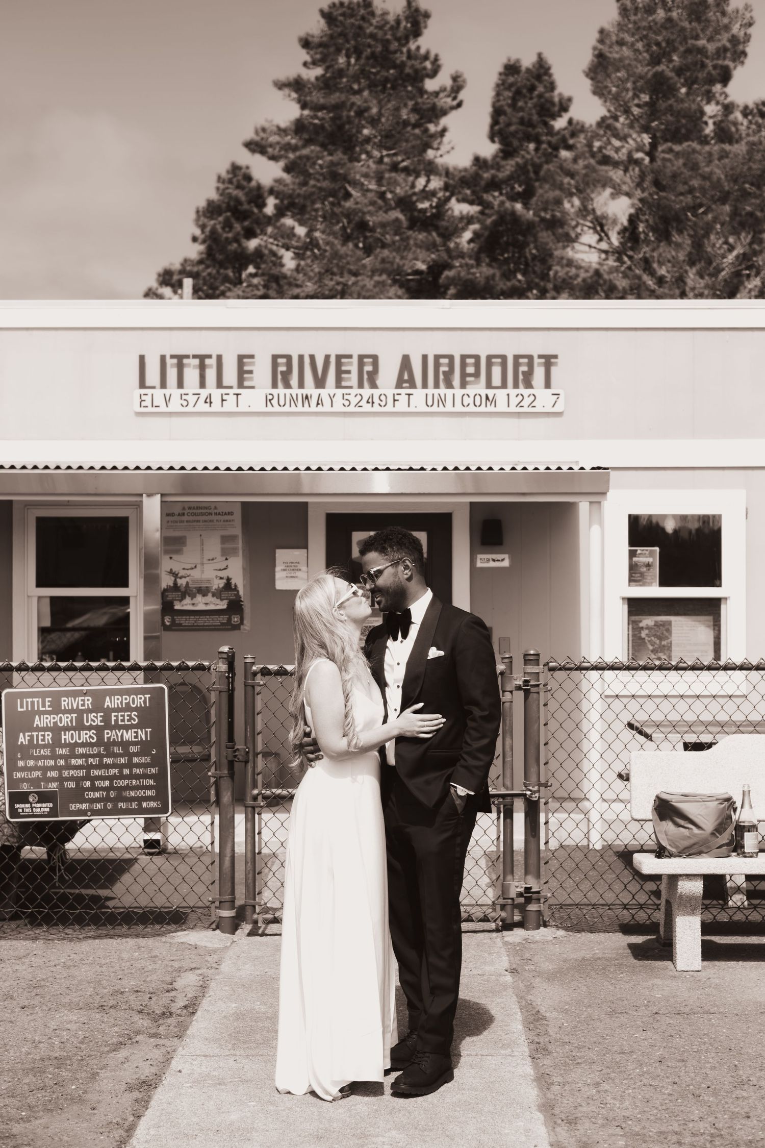 Bride and groom share a romantic moment outside Little River Airport in a sepia-toned wedding photo.