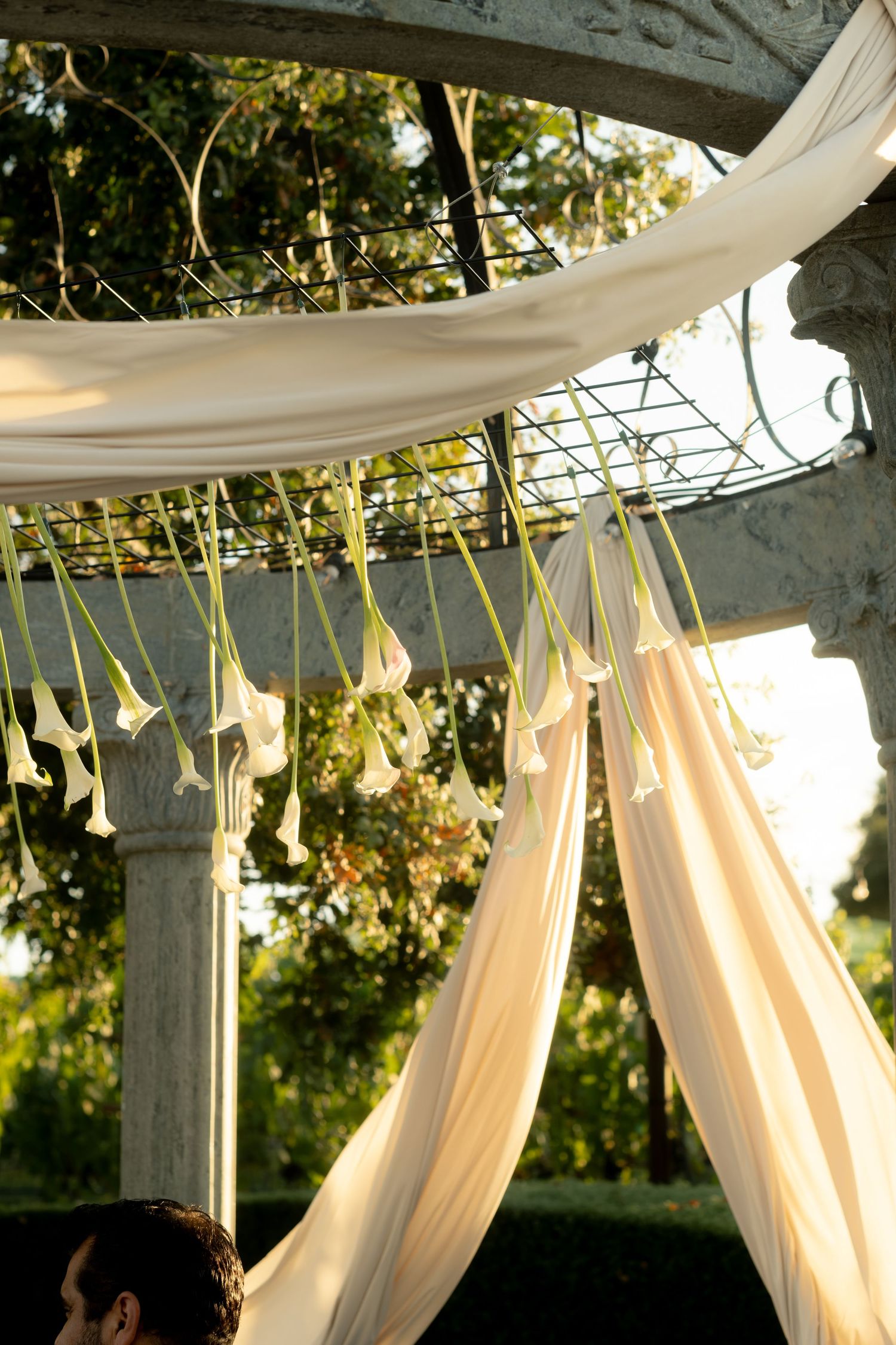 Romantic wedding ceremony chuppah draped in ivory fabric adorned with hanging white calla lilies outdoors.