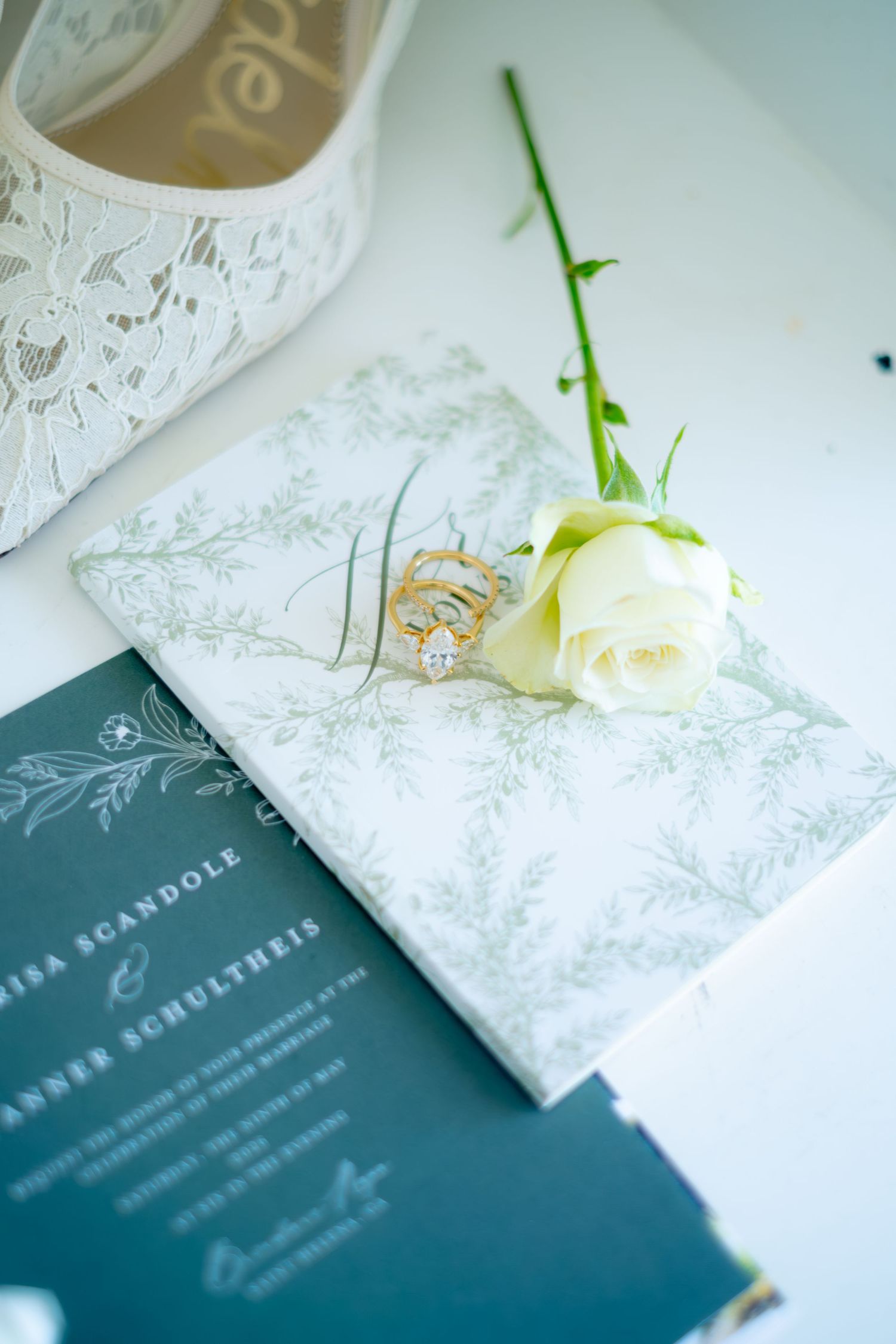 Wedding invitation suite with a white rose and gold diamond engagement ring on a floral design card.