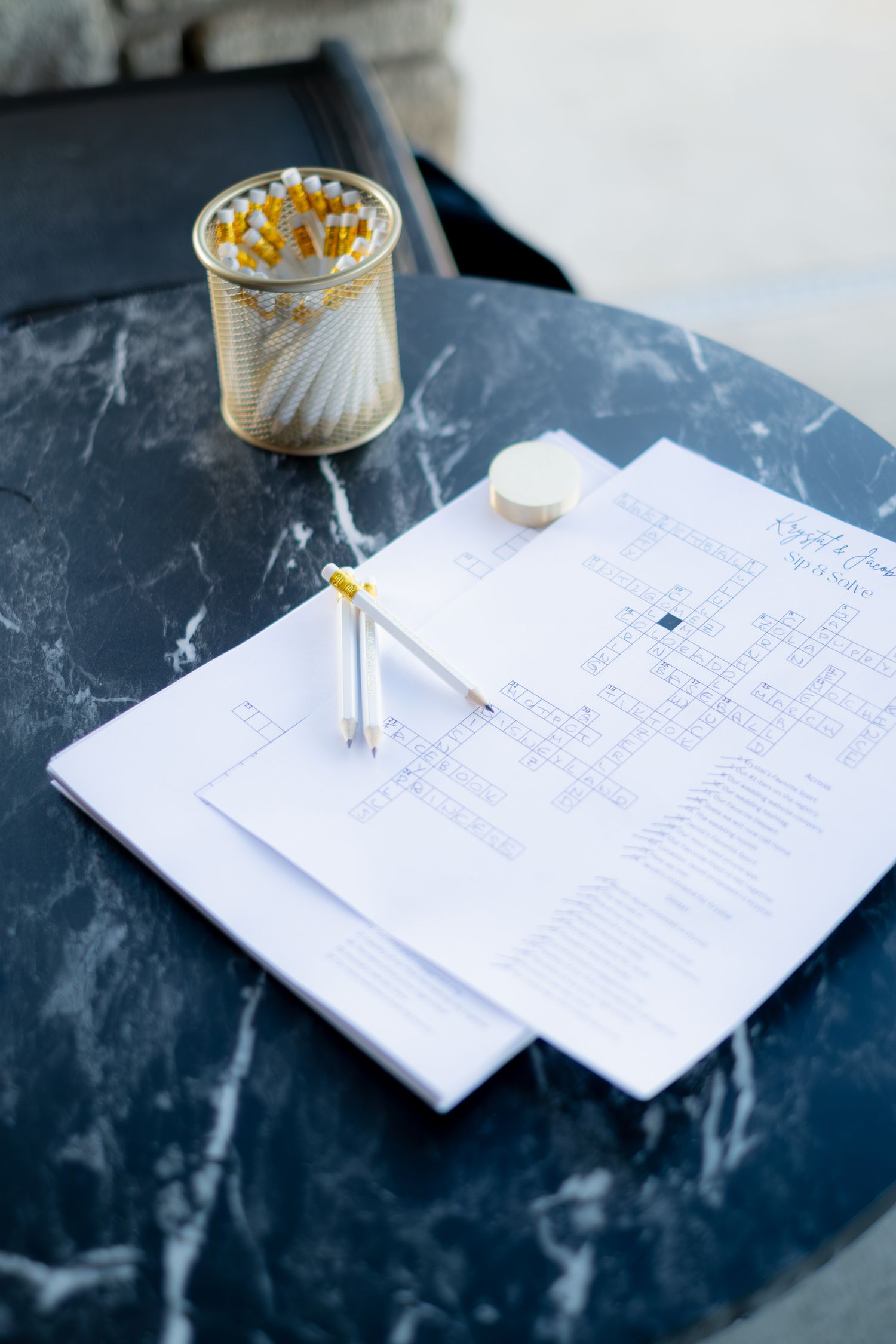 Wedding crossword puzzle activity sheets with pencils on marble table at outdoor reception.