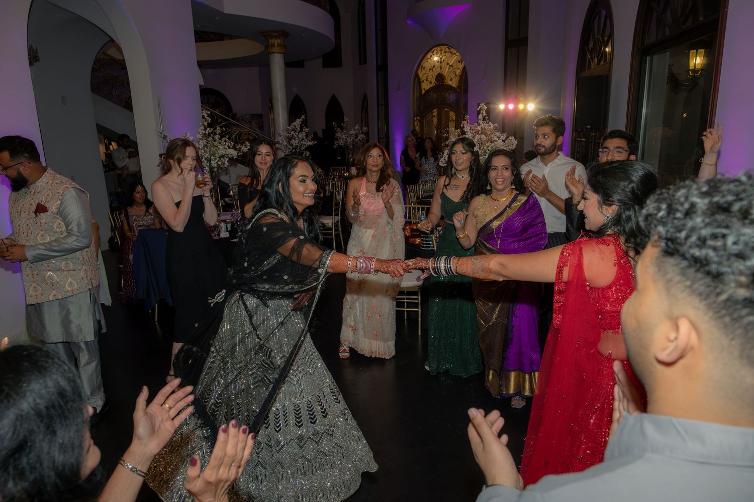 Guests in traditional Indian attire celebrate on a vibrant wedding reception dance floor.