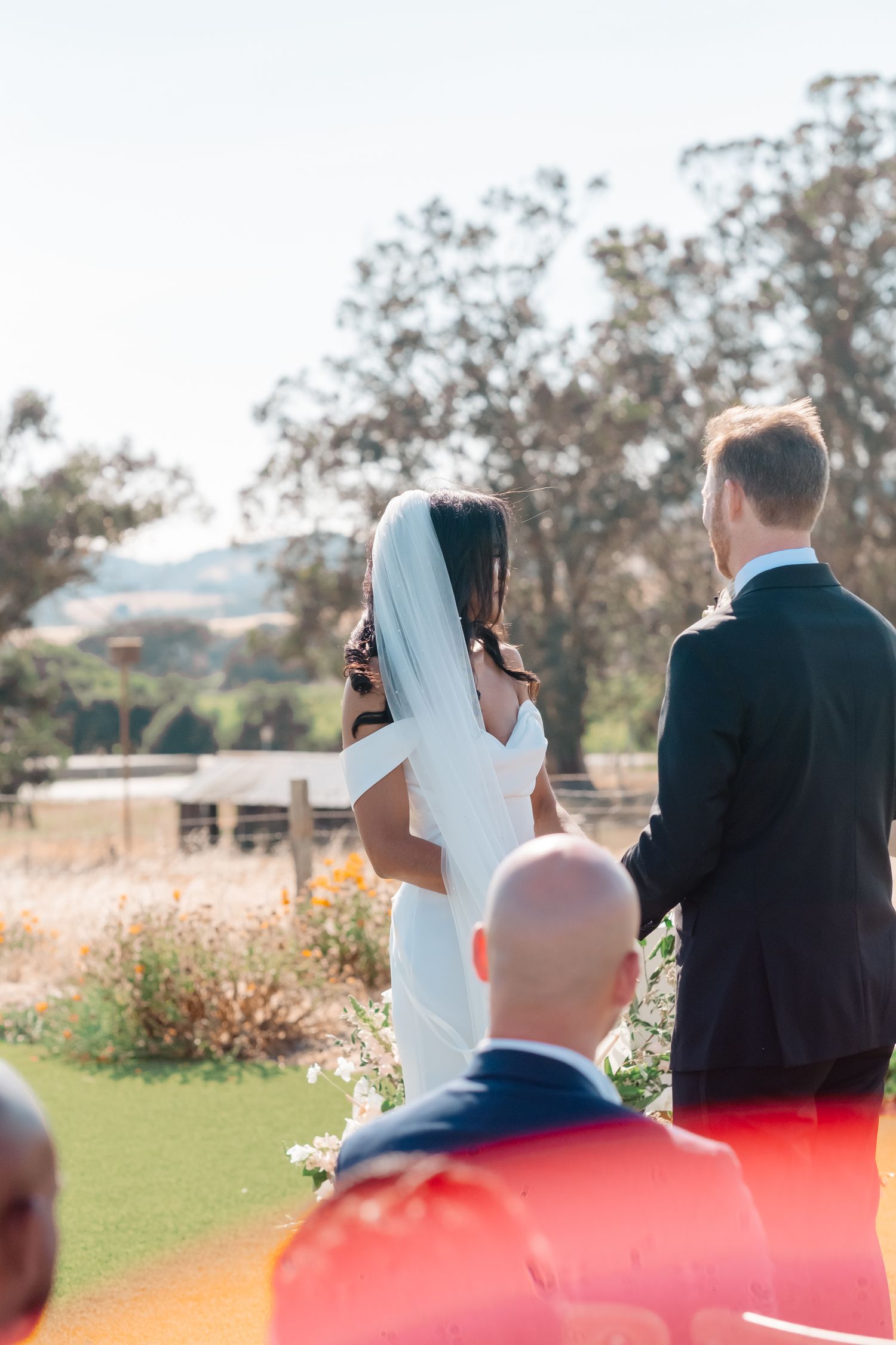 Bride and groom exchange vows at an outdoor wedding ceremony with scenic hillside views.